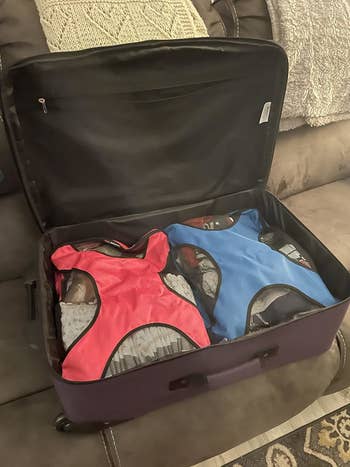 Open suitcase on a couch, packed with two compression bags holding clothes, one red and one blue