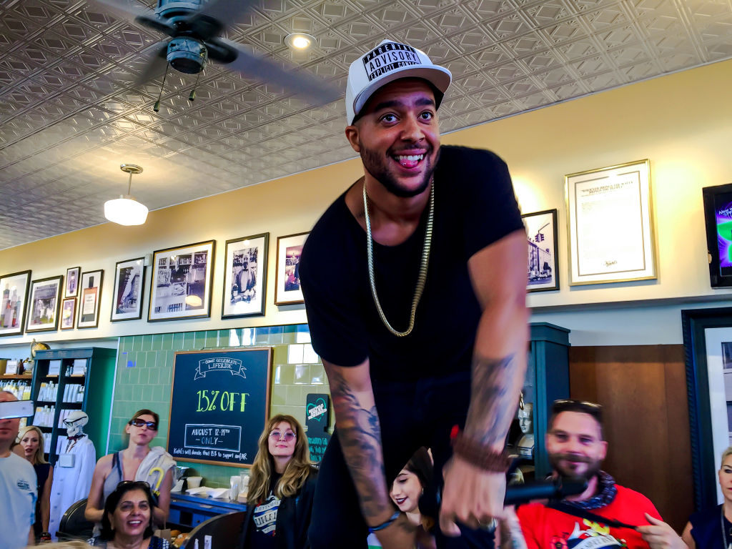 Willy William smiling and standing on a counter in a lively atmosphere, surrounded by fans inside a store