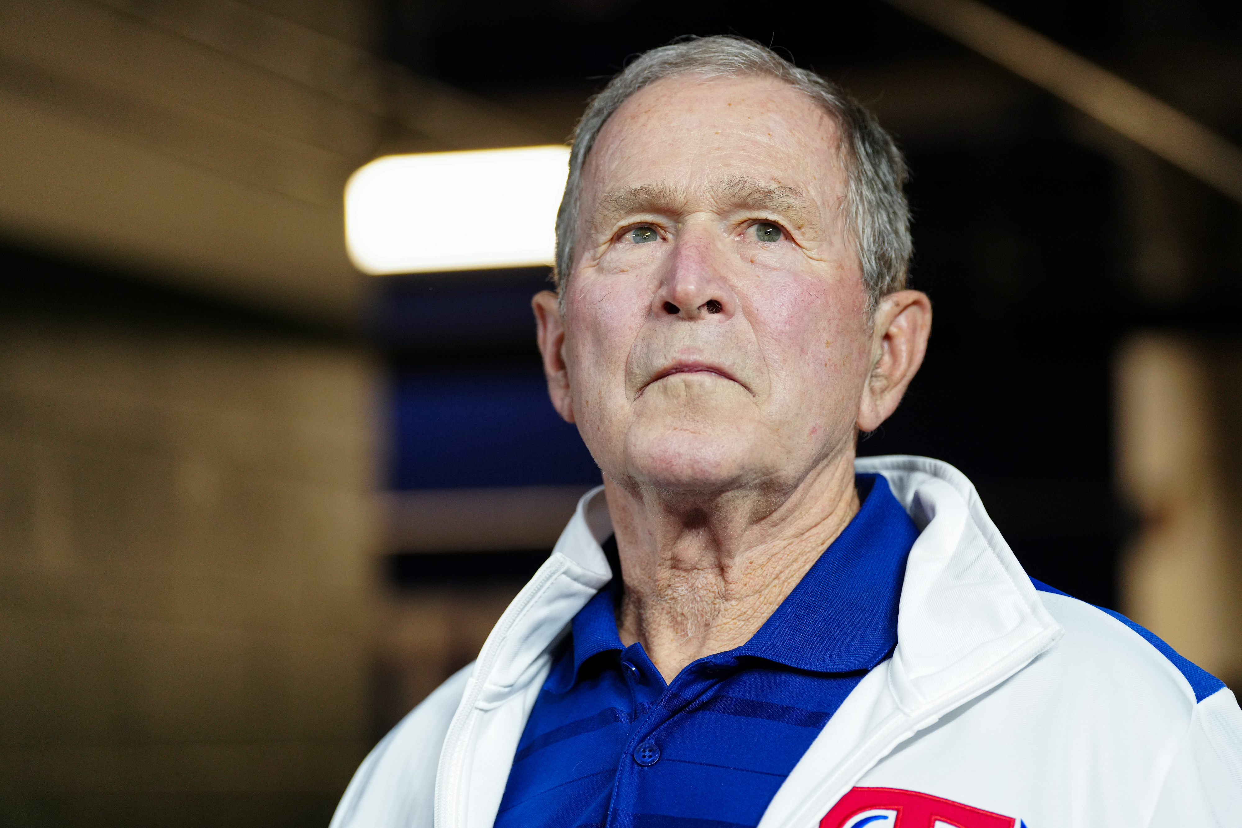 George W. Bush in a blue polo shirt and a white jacket, looking into the distance
