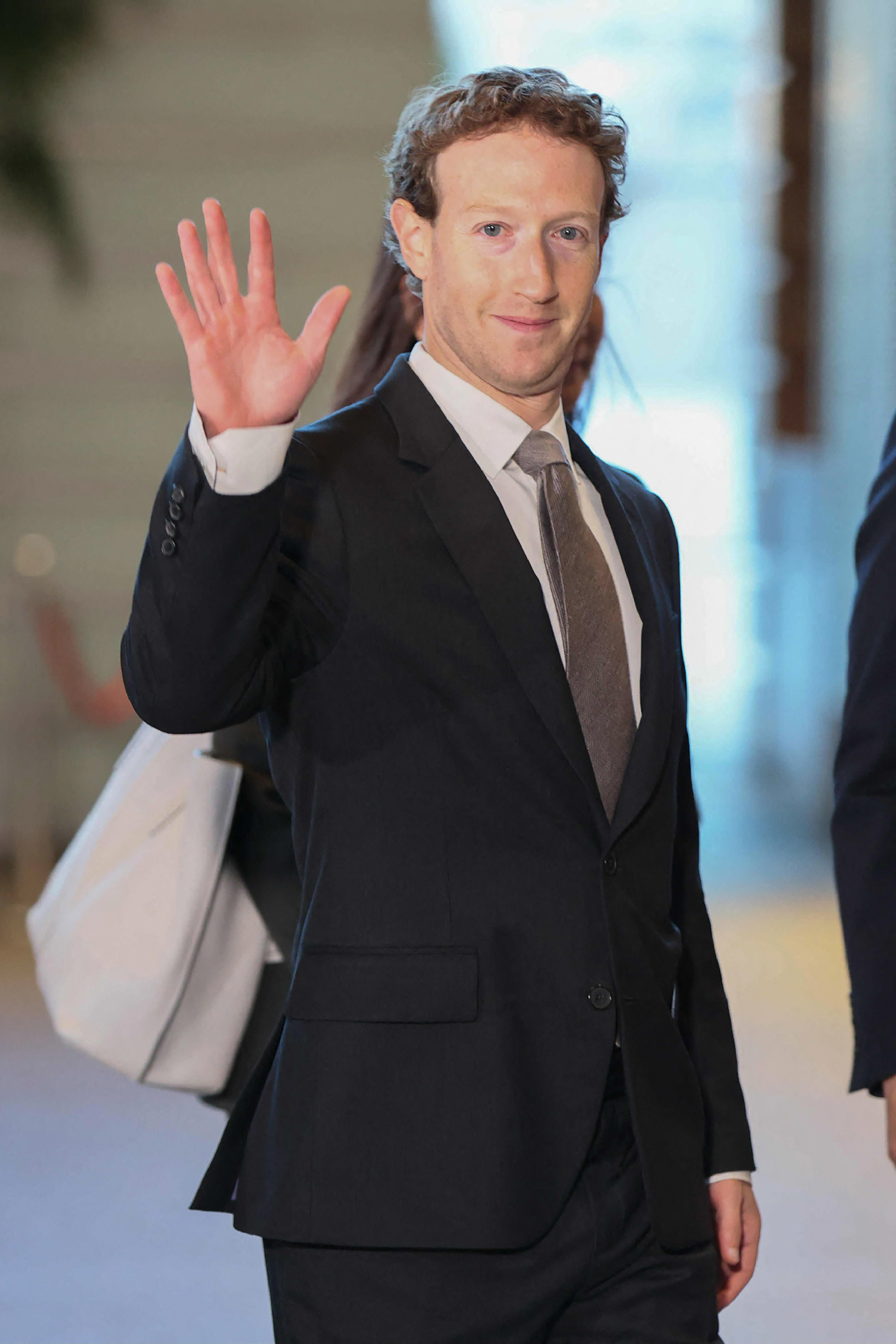 Mark Zuckerberg in a business suit waving at the camera