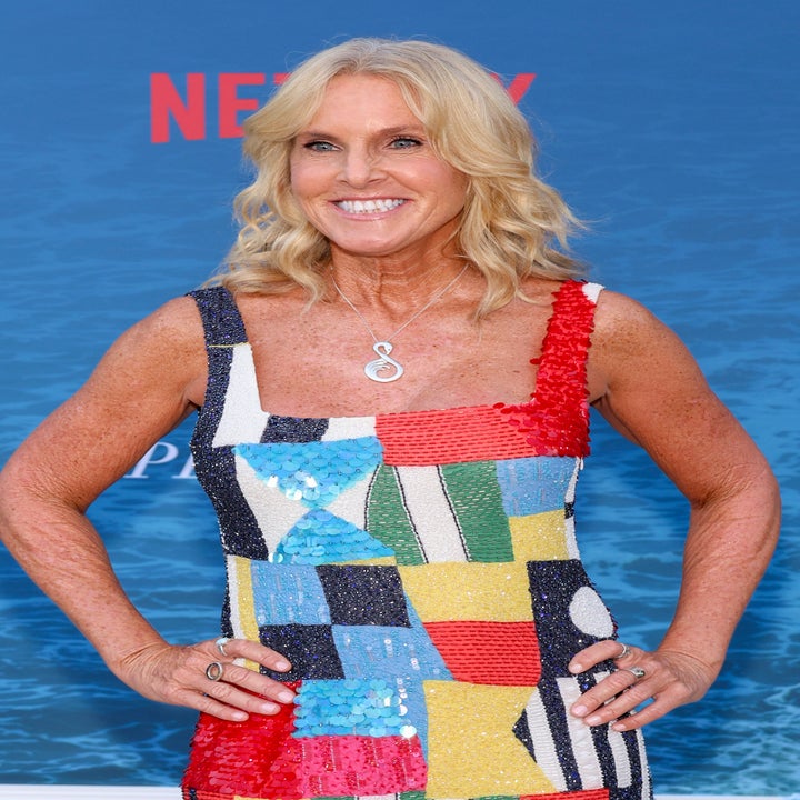 Elin Hilderbrand in a colorful patchwork-style dress poses on a red carpet at a Netflix event for "The Perfect Couple."