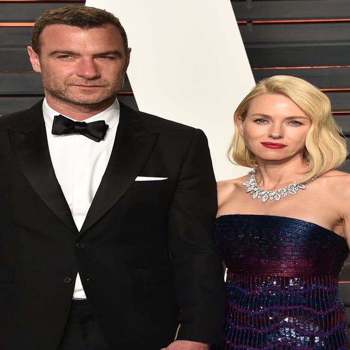 Liev Schreiber in a black tuxedo and Naomi Watts in a strapless sequined gown at a red carpet event, holding hands and posing for photos