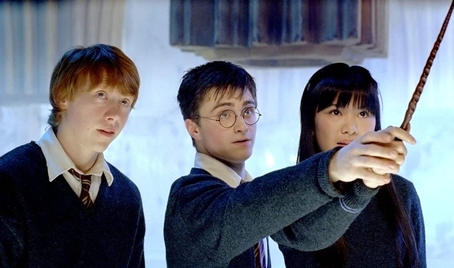 Rupert Grint, Daniel Radcliffe, and Katie Leung in Hogwarts uniforms with wands in a scene from Harry Potter