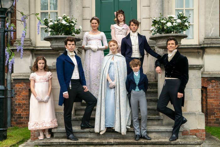 The image shows several people from the Bridgerton series dressed in elegant Regency-era attire, posed on steps outside a grand building