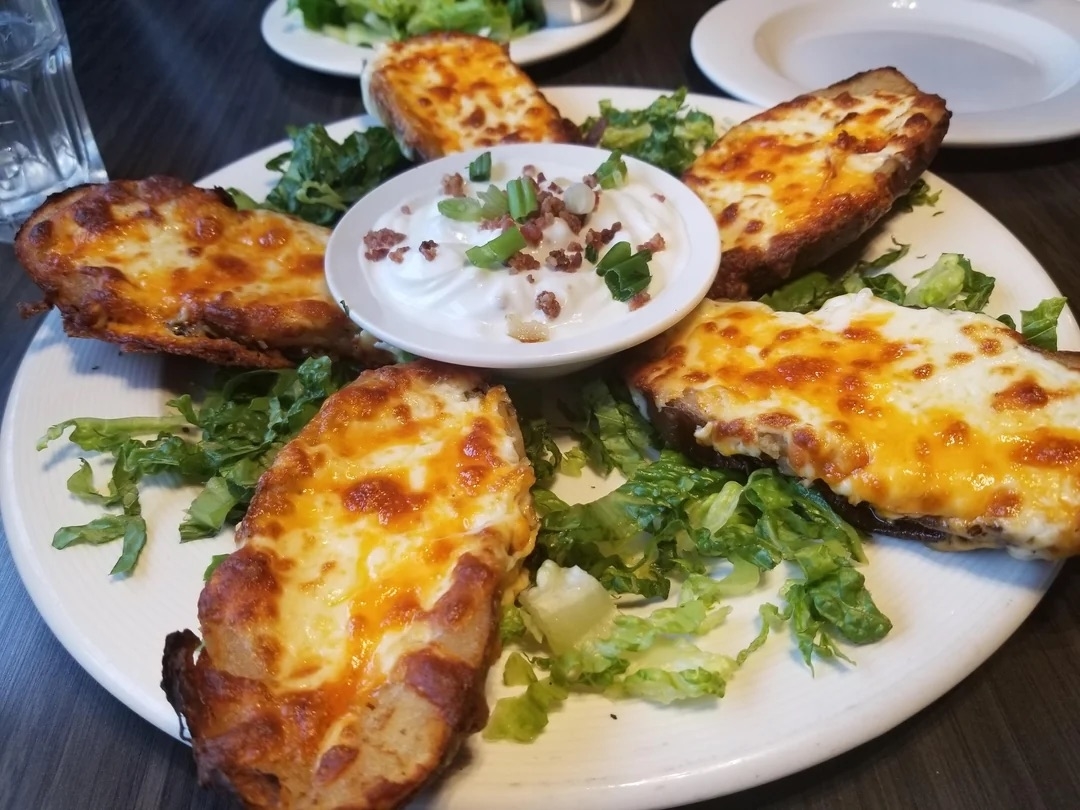 A plate of loaded potato skins with melted cheese, bacon bits, and green onions, surrounding a bowl of sour cream, garnished with lettuce