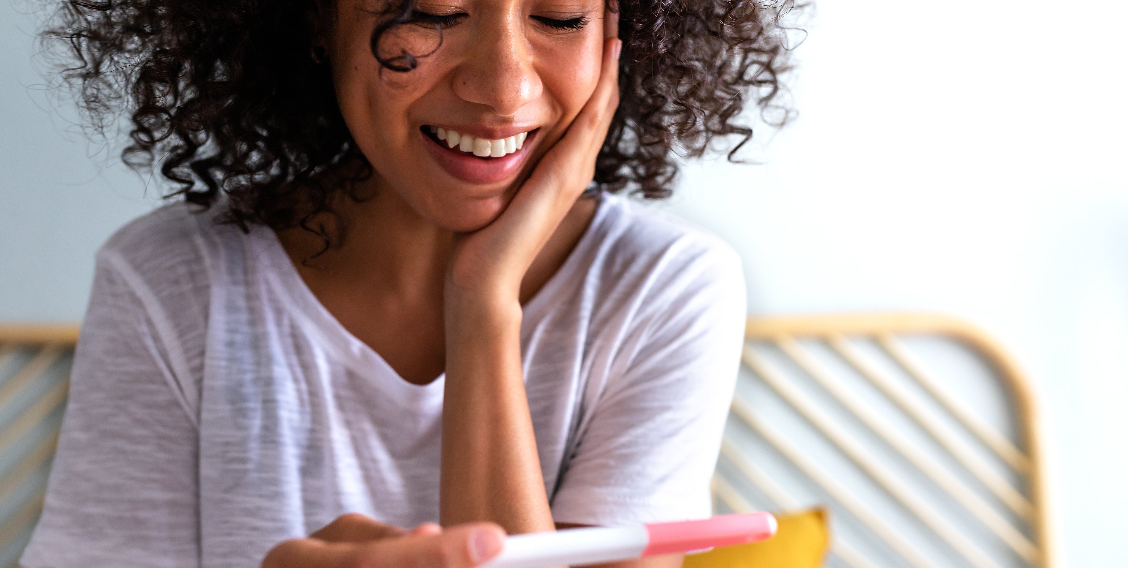 A person with curly hair smiling emotionally while holding a pregnancy test