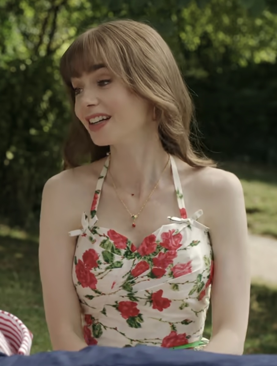 Lily Collins wearing a floral pattern halter dress, smiling while sitting outdoors, in a garden setting