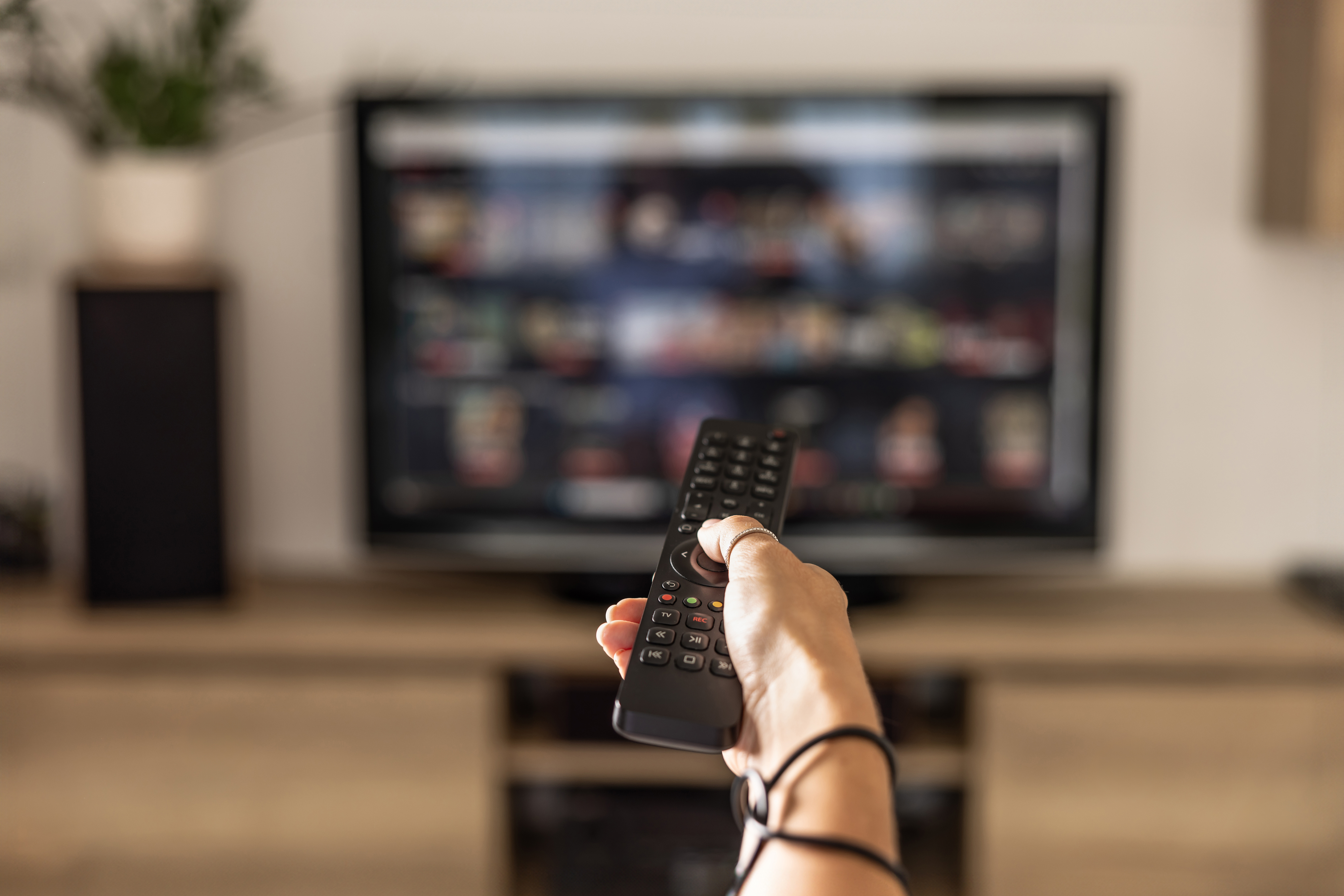 A person points a remote control at a television with a streaming service menu on the screen in a living room