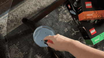 A hand starts building a LEGO ball maze from the LEGO Ideas set on a table