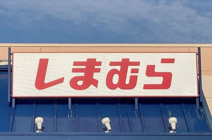 Storefront with a sign in Japanese characters displayed above it. The sign reads &ldquo;しまむら.&rdquo; A handicap parking sign is visible in the corner