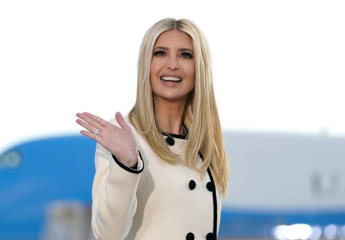 Ivanka Trump waves and smiles while wearing a stylish long-sleeved coat with black buttons. A blurred background of what appears to be an airplane is visible