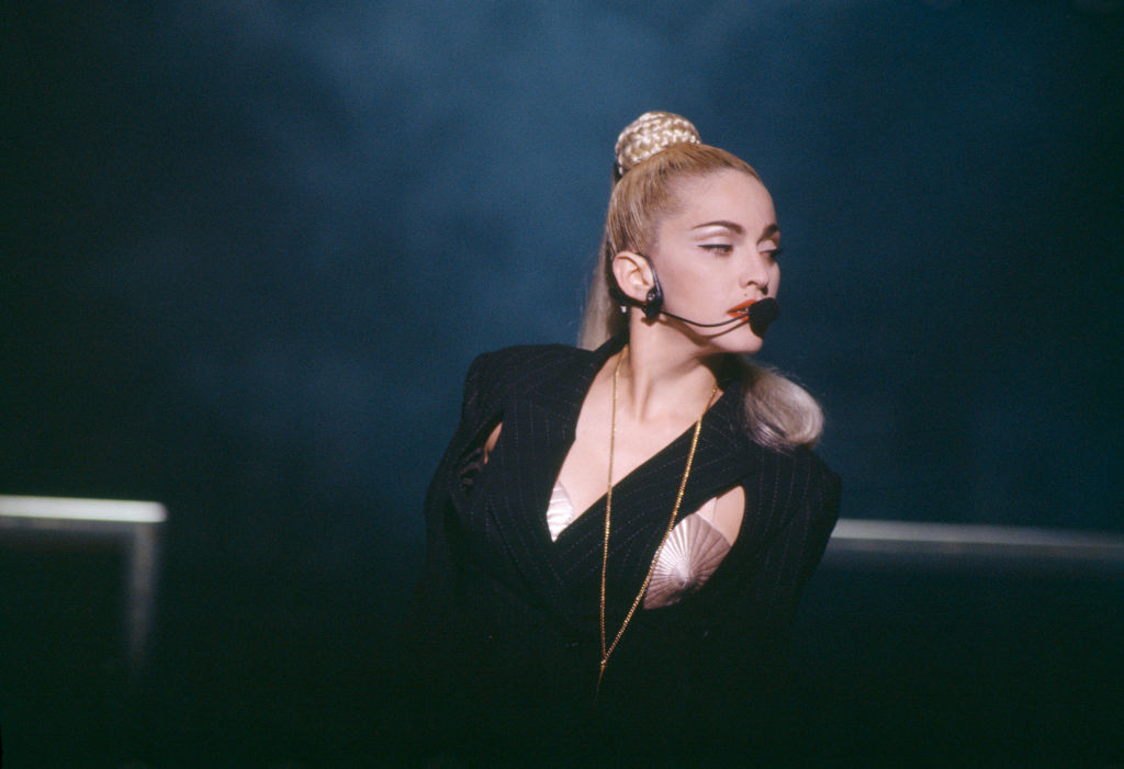 Madonna performs wearing a cone bra top and dark blazer with a headset microphone