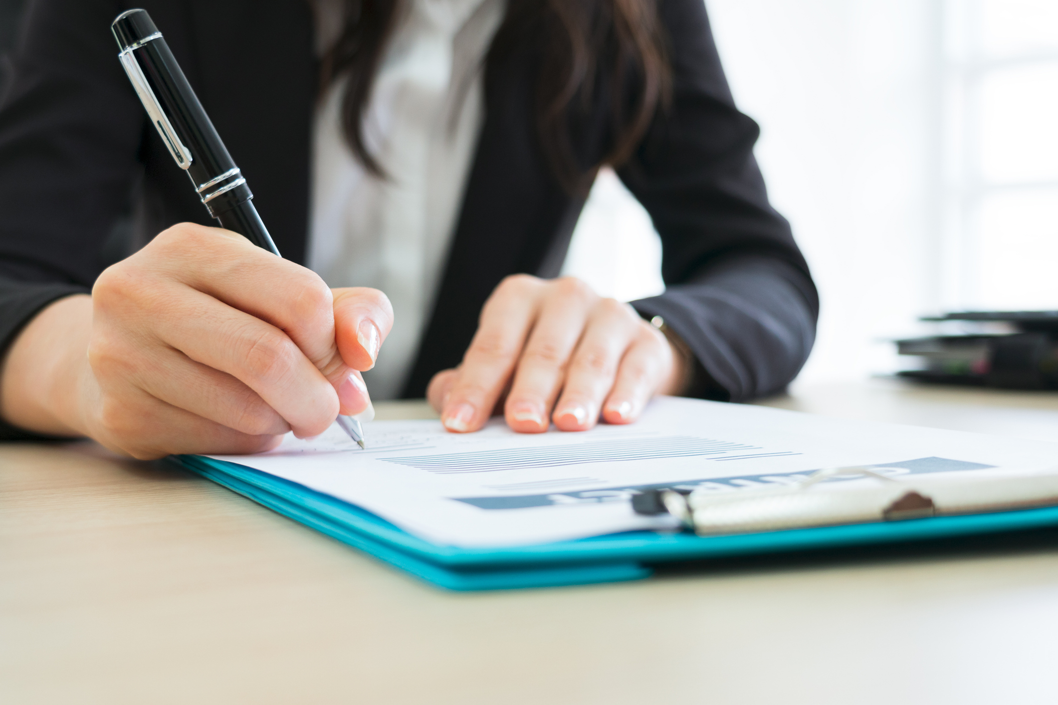 A person in a suit signs a document with a pen, indicating a business or financial setting. The article is categorized under Work &amp;amp; Money