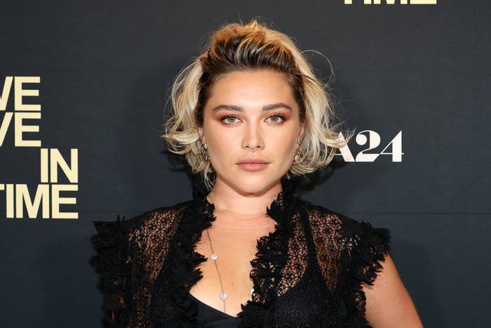 Florence Pugh at an event, wearing a lace overlay top with a deep neckline and layered necklace