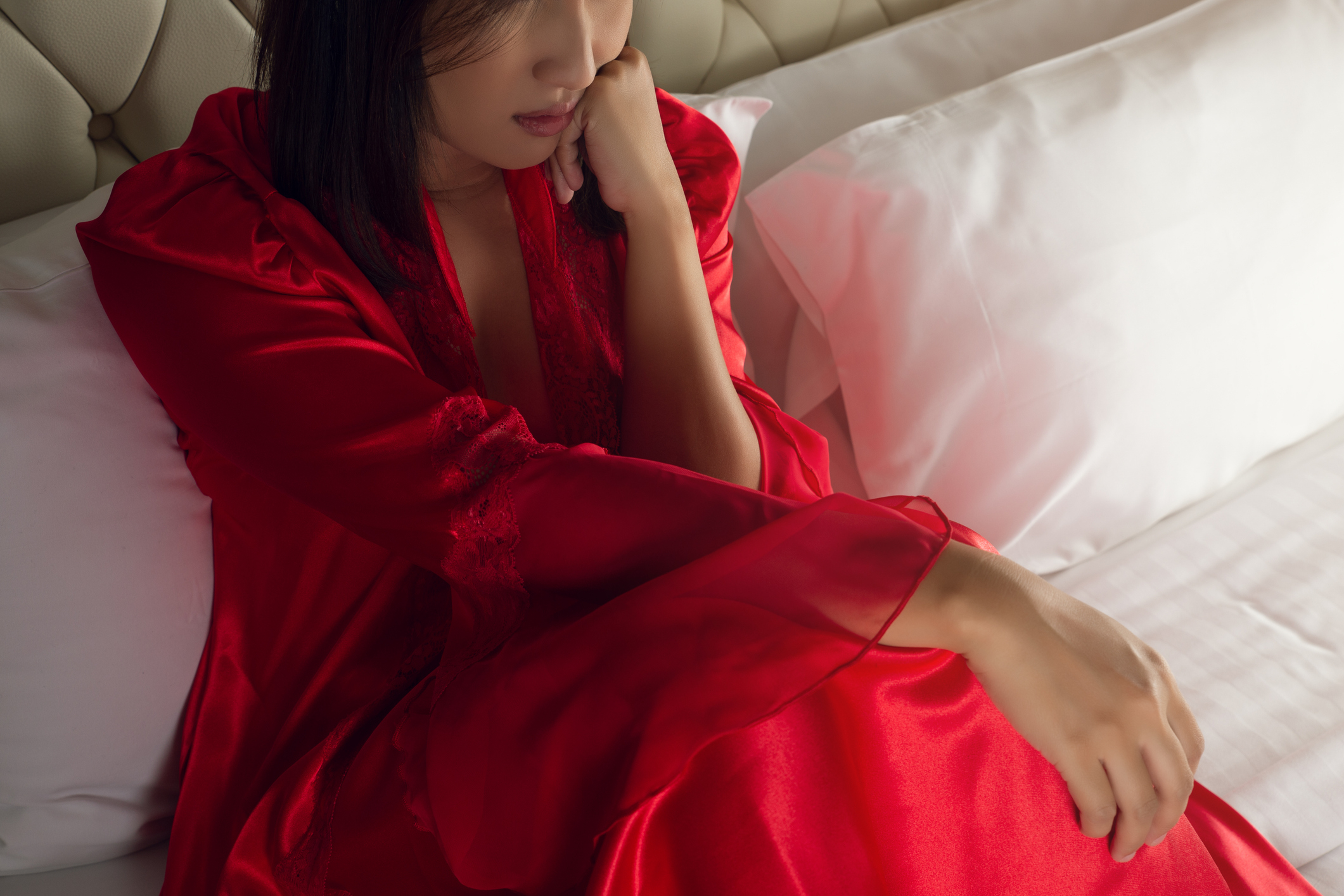 A person seated on a bed, wearing a long, silky robe, looking thoughtful with their arm resting on their leg