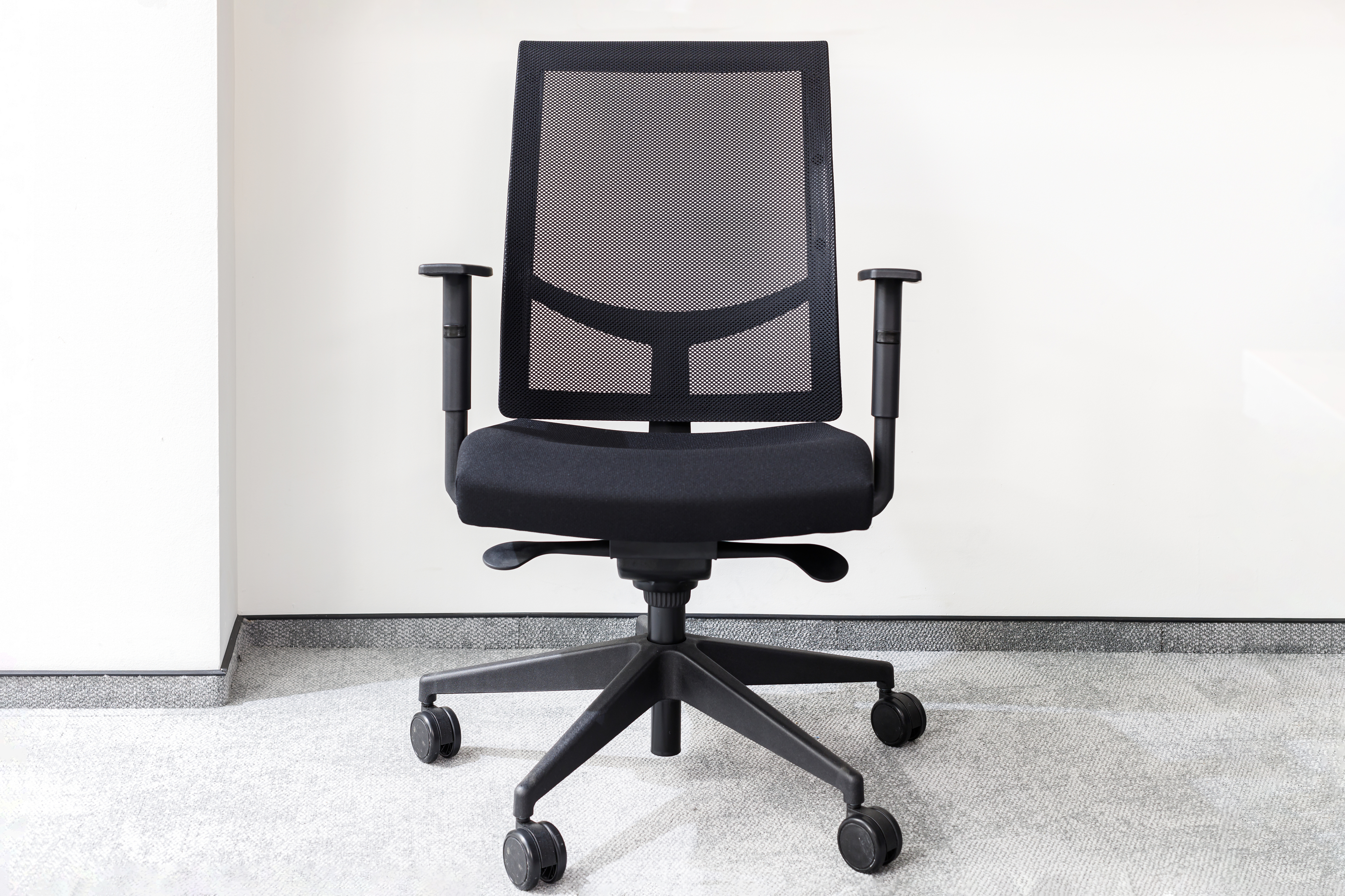 Ergonomic office chair with a mesh backrest, adjustable armrests, and a five-wheel base on a carpeted floor