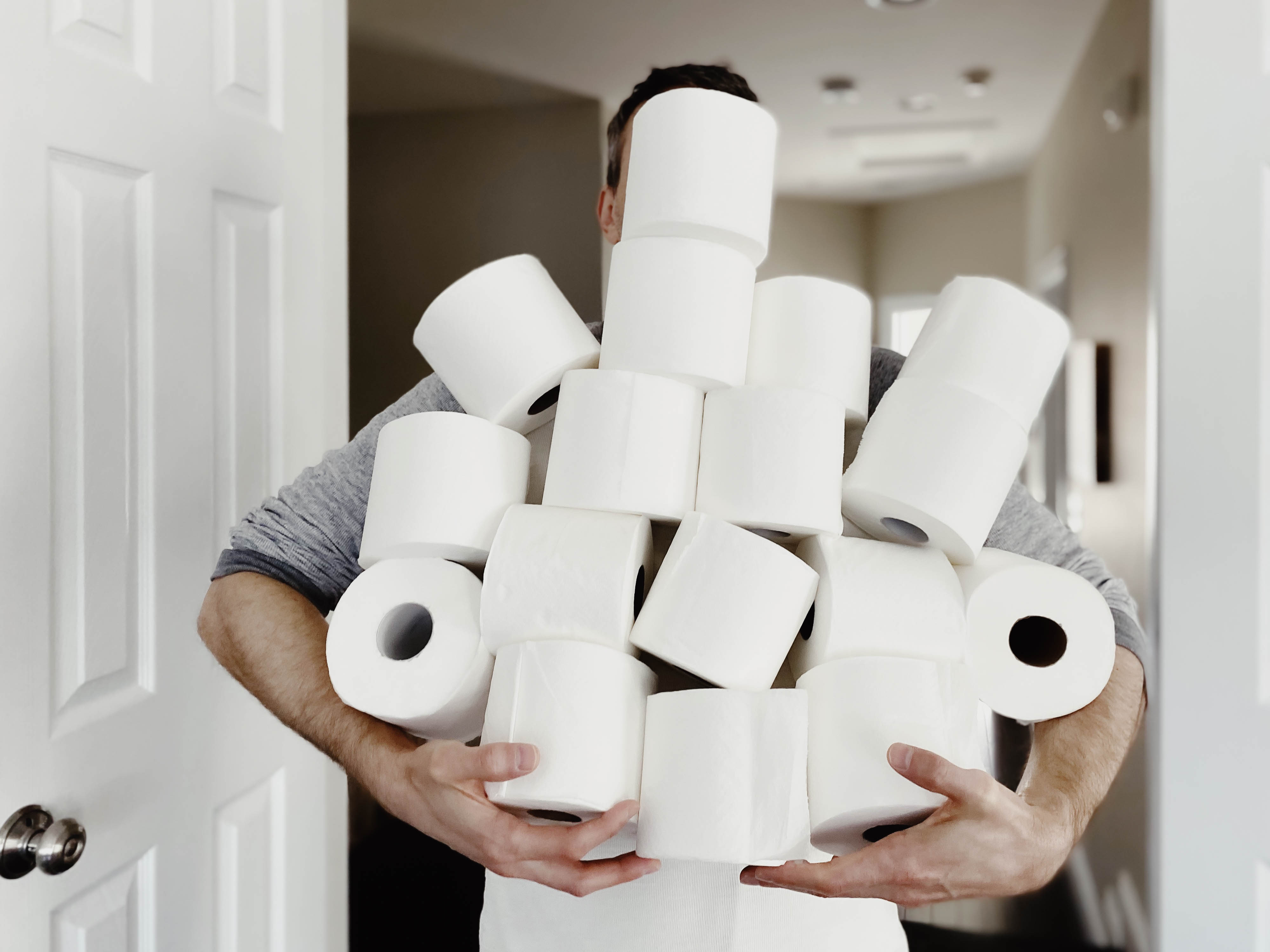 A person holding a large stack of toilet paper rolls, obscuring their face and torso