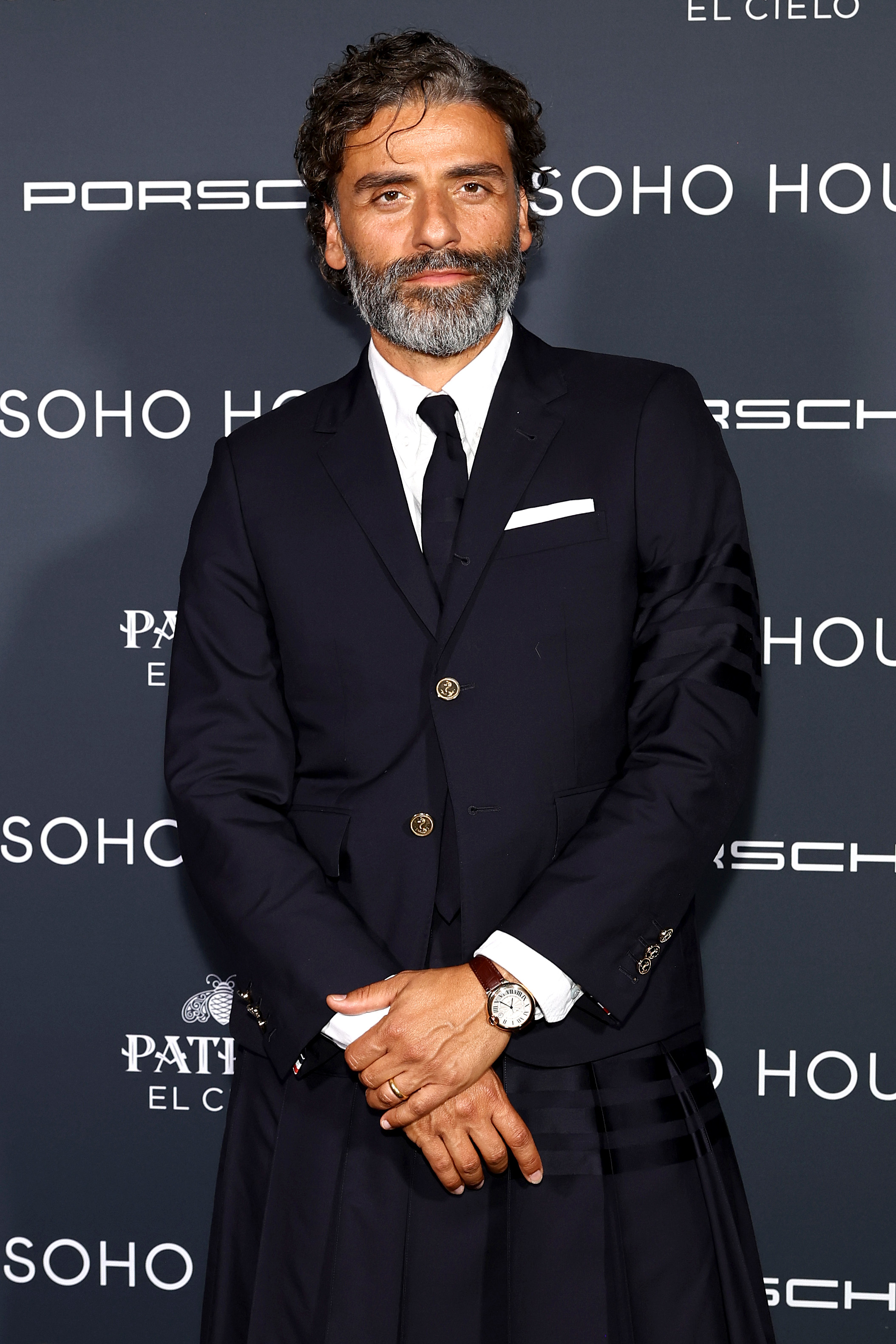 Oscar Isaac in a tailored dark suit with a tie, standing on the red carpet at a Porsche Soho House event