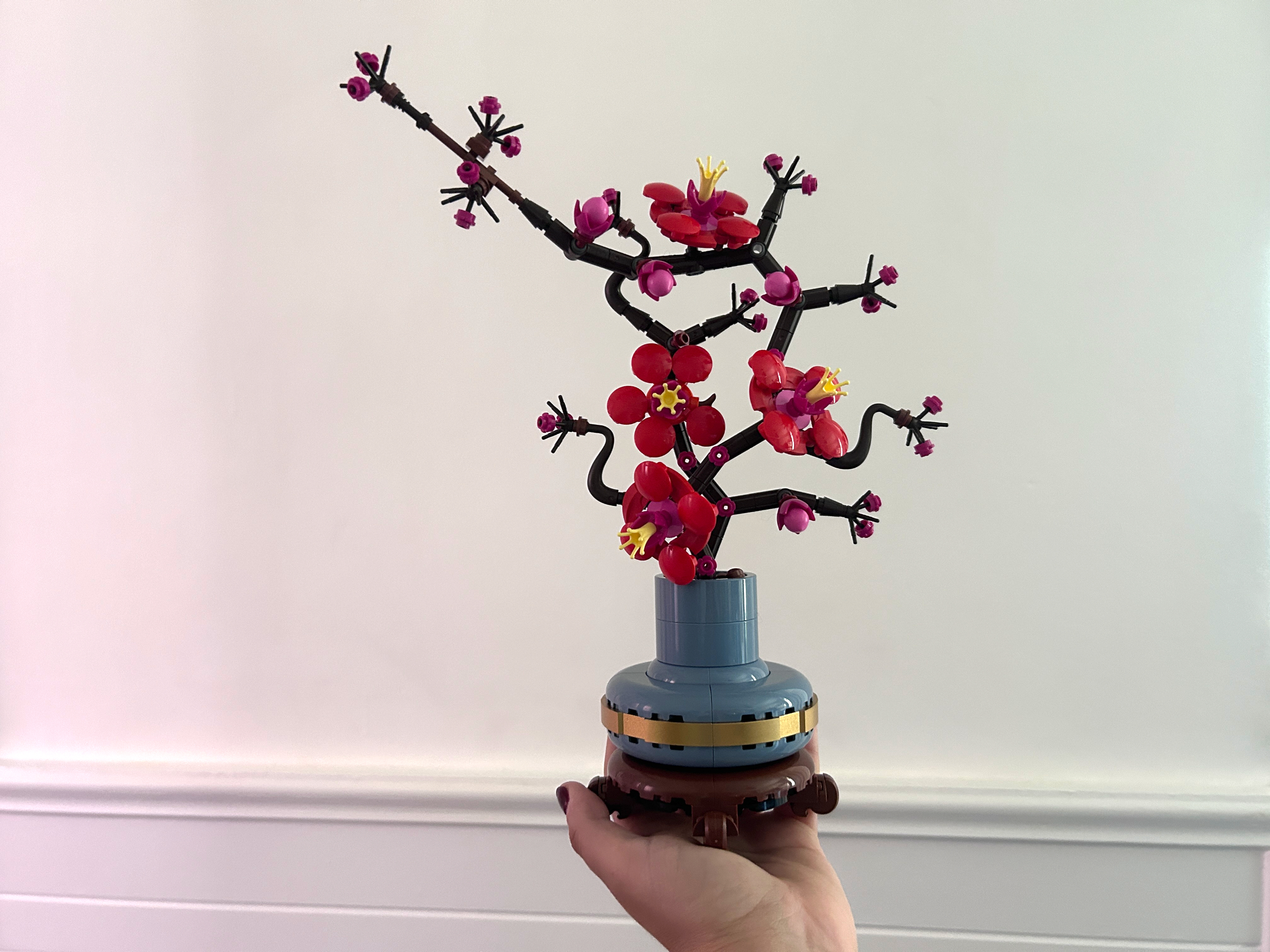 A hand holding a small, detailed LEGO sculpture of a blossoming cherry tree branch