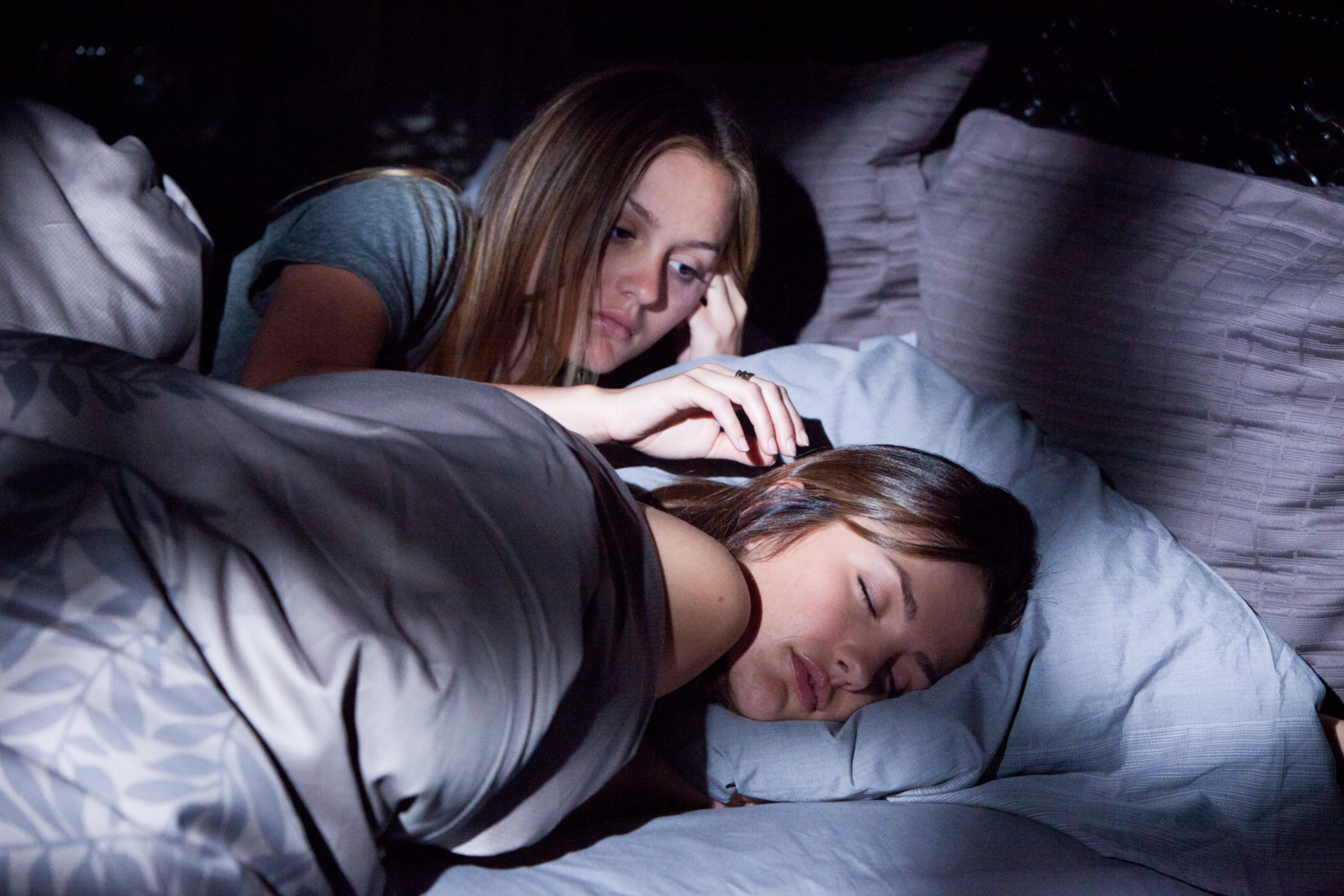 Leighton Meester and Minka Kelly lie in bed; Leighton looks at Minka who is asleep