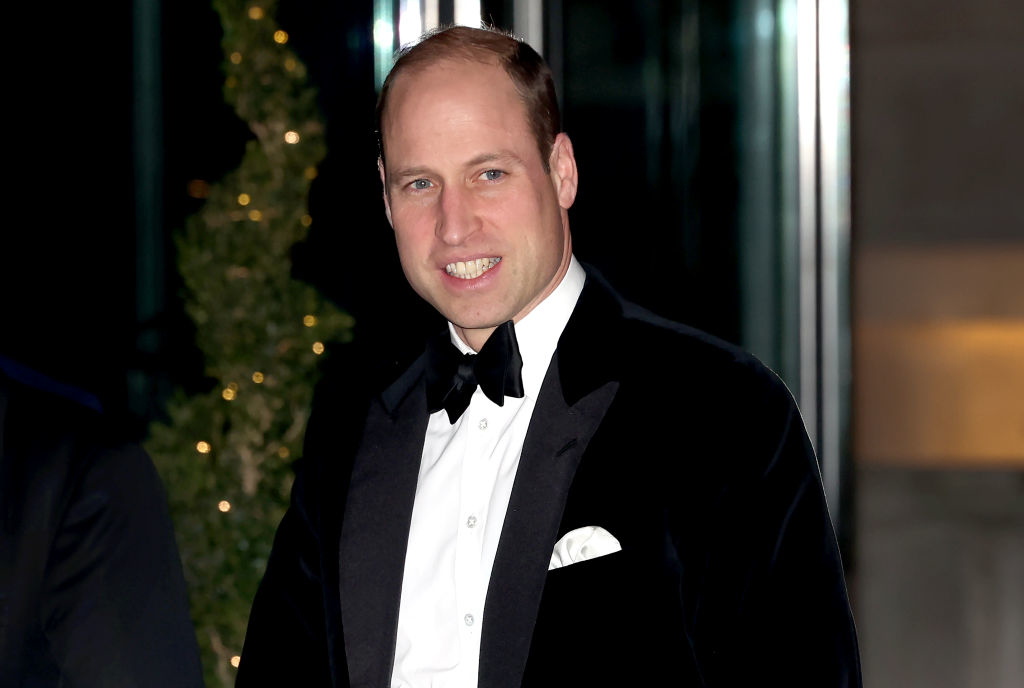 Prince William smiles while wearing a black tuxedo and bow tie at an evening event