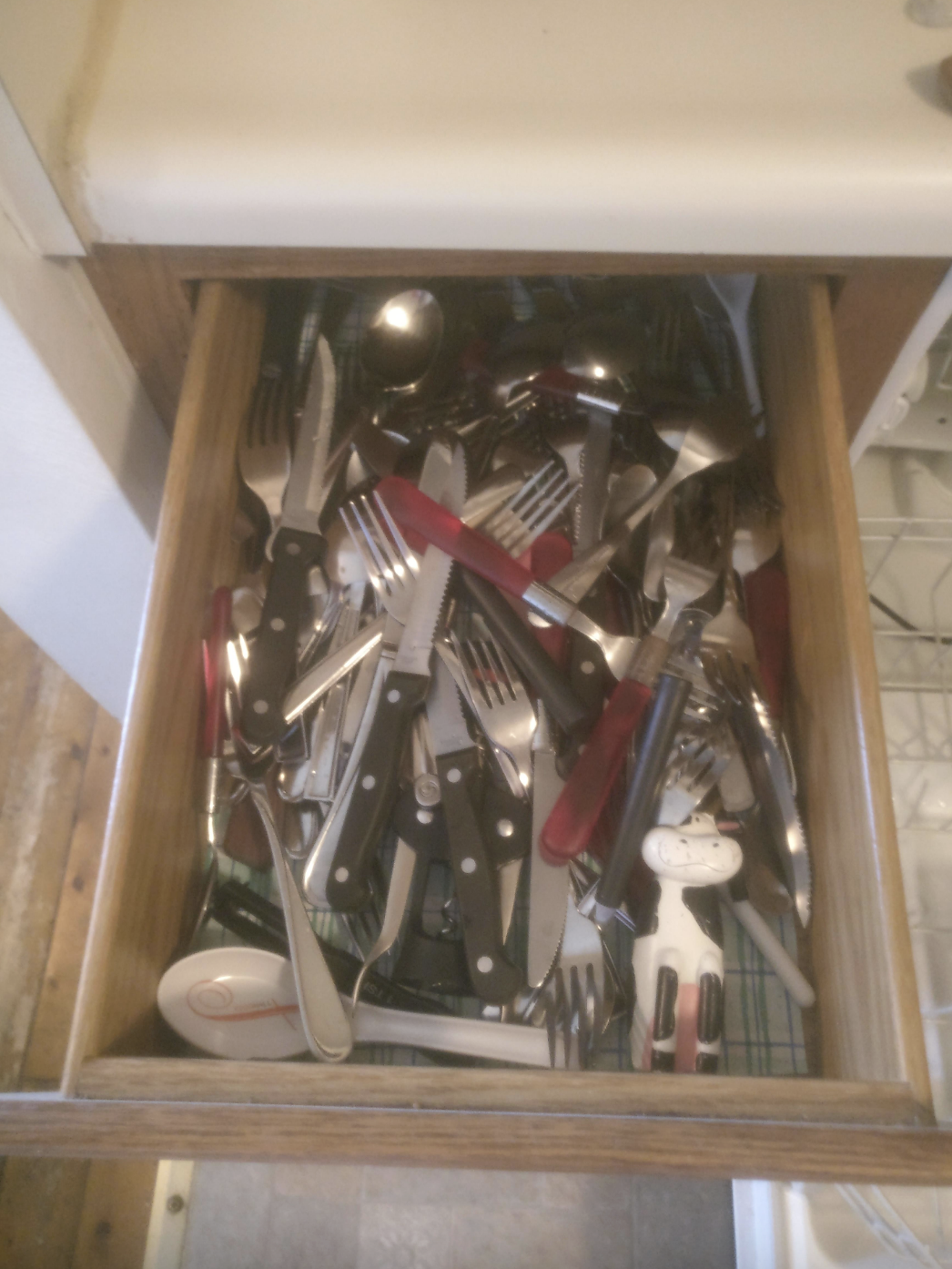 A kitchen drawer filled with various utensils including forks, knives, spoons, and other kitchen tools, in a disorganized manner
