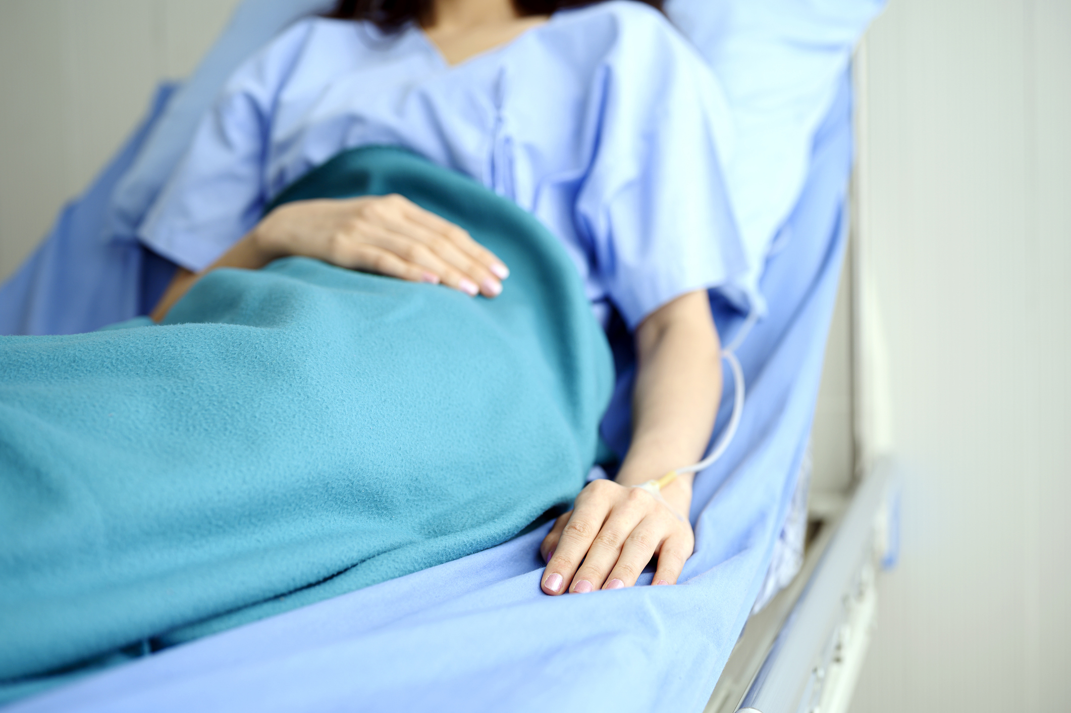 Person in a hospital bed with their hand resting on the blanket, representing themes of care, health, and recovery