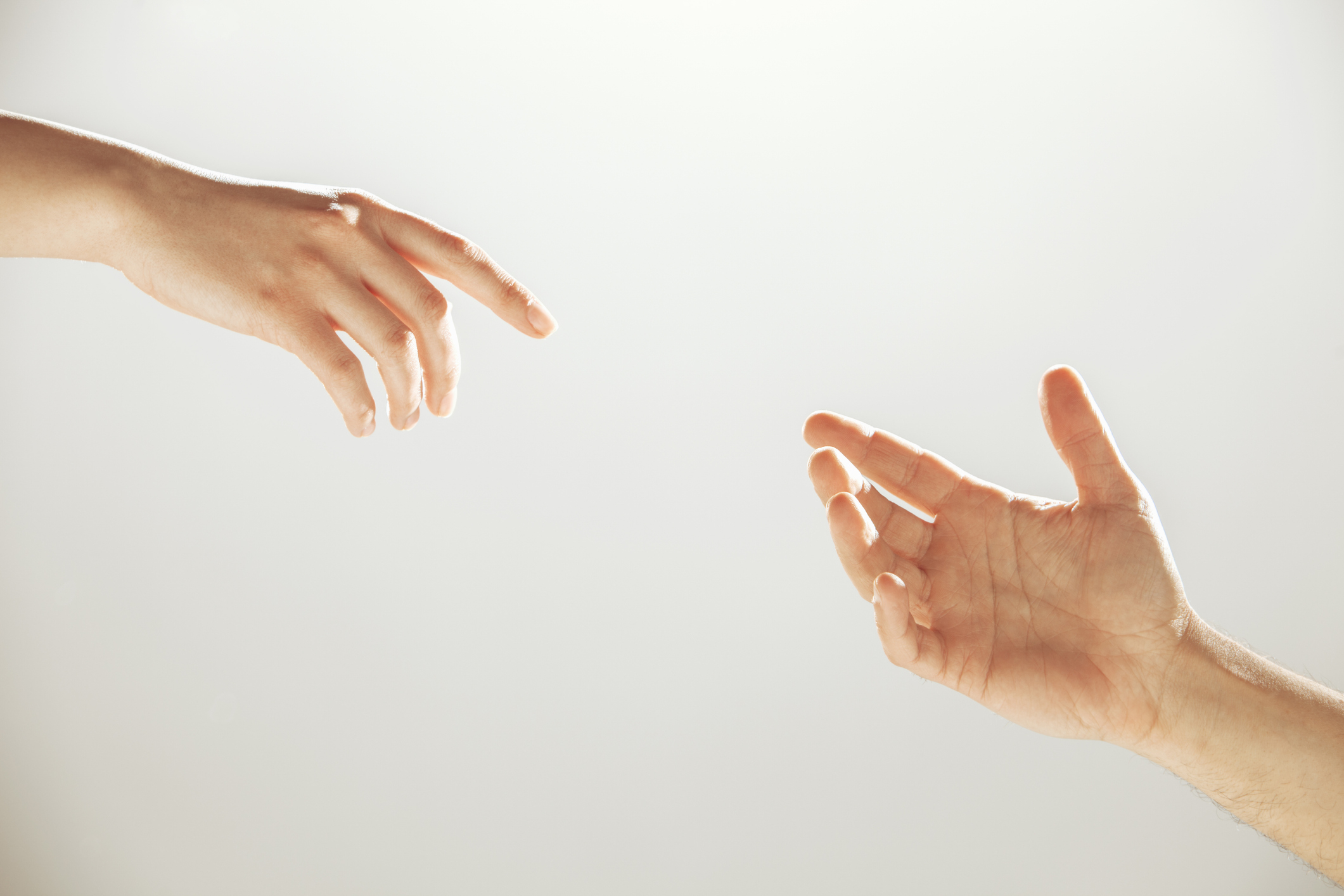 Two hands reaching out towards each other, with fingers almost touching, against a neutral background