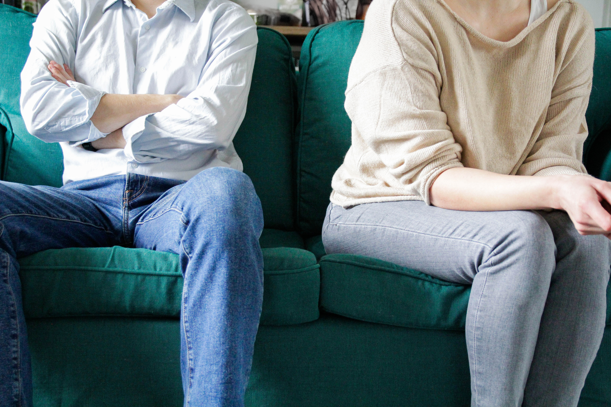 Two people sitting on a couch with arms crossed, facing away from each other. They appear to be in a disagreement