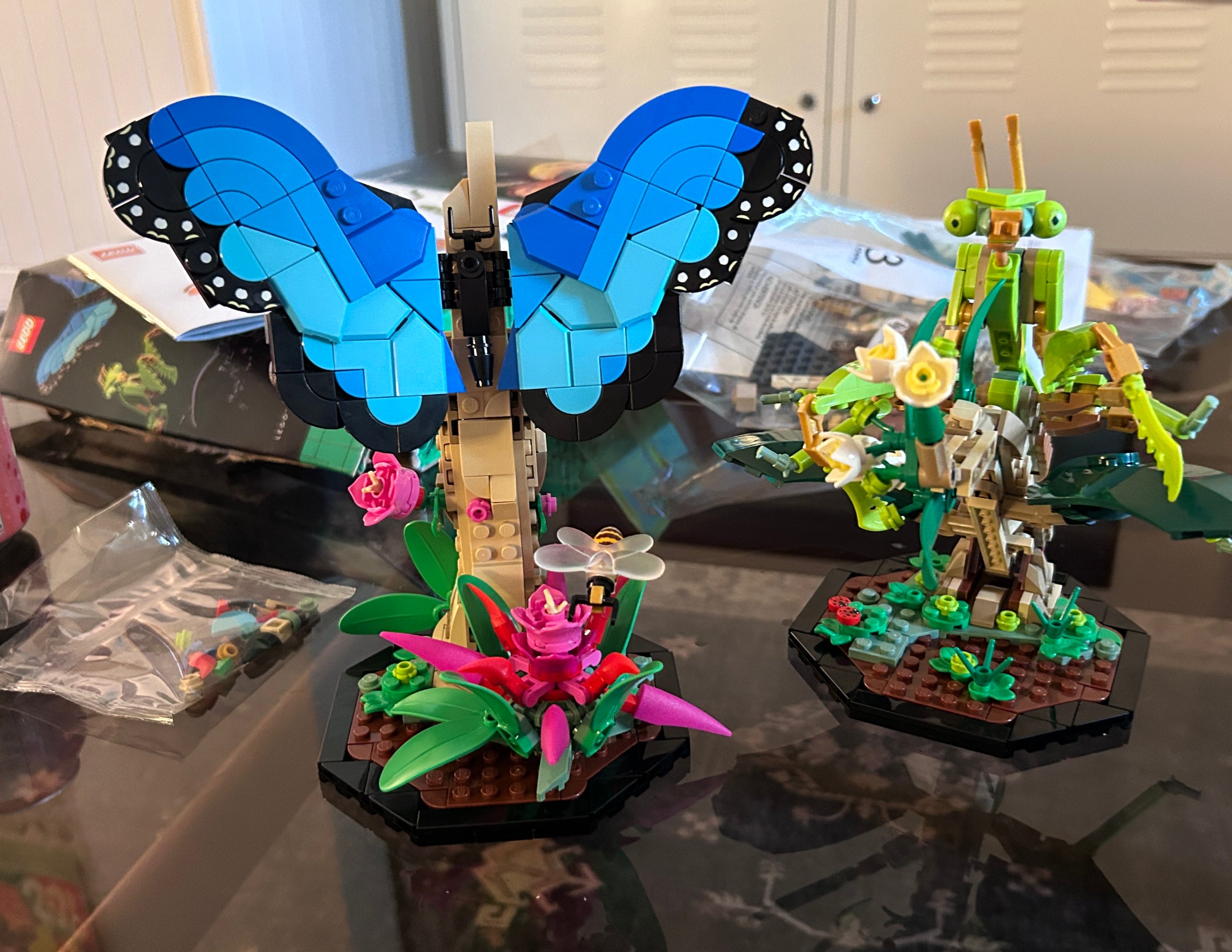 Lego models of a blue butterfly and a green praying mantis displayed on a table next to a soda can and Lego packaging
