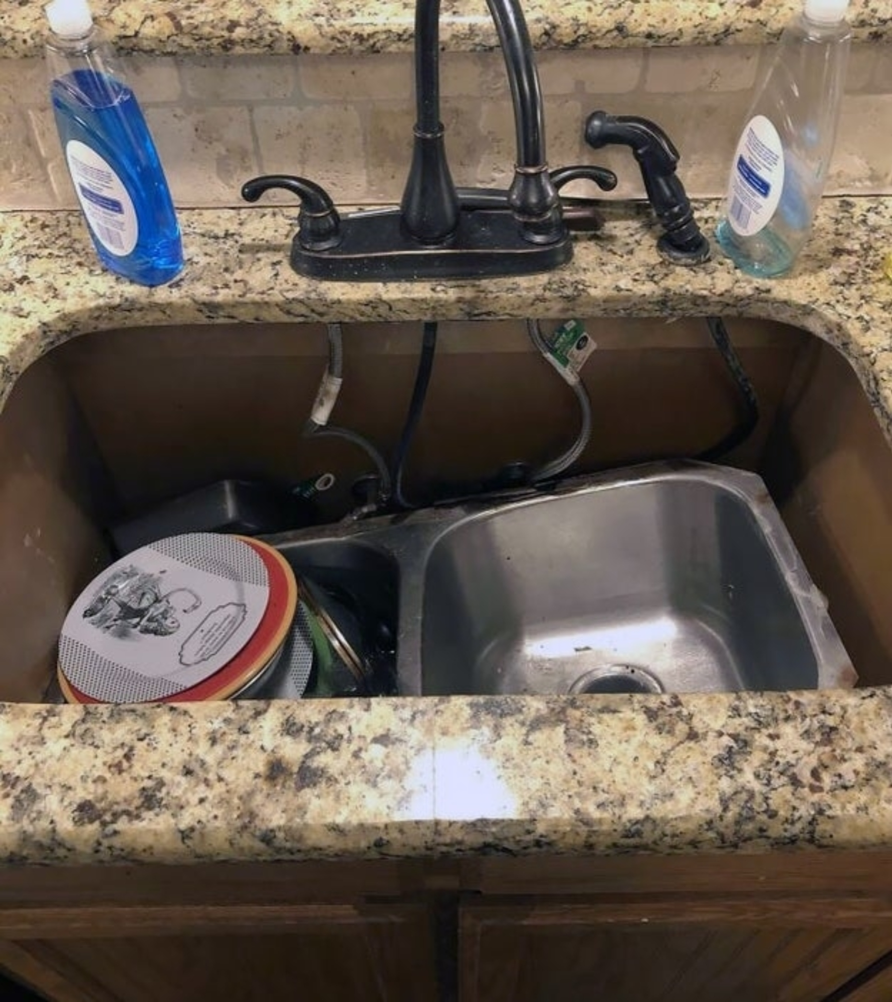 A kitchen sink thats fallen into it's basin with unwashed dishes, including a pot, plates, and bowls