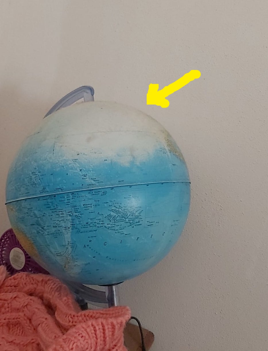 A globe on a wooden table that is missing part of the world map because it was rubbed off