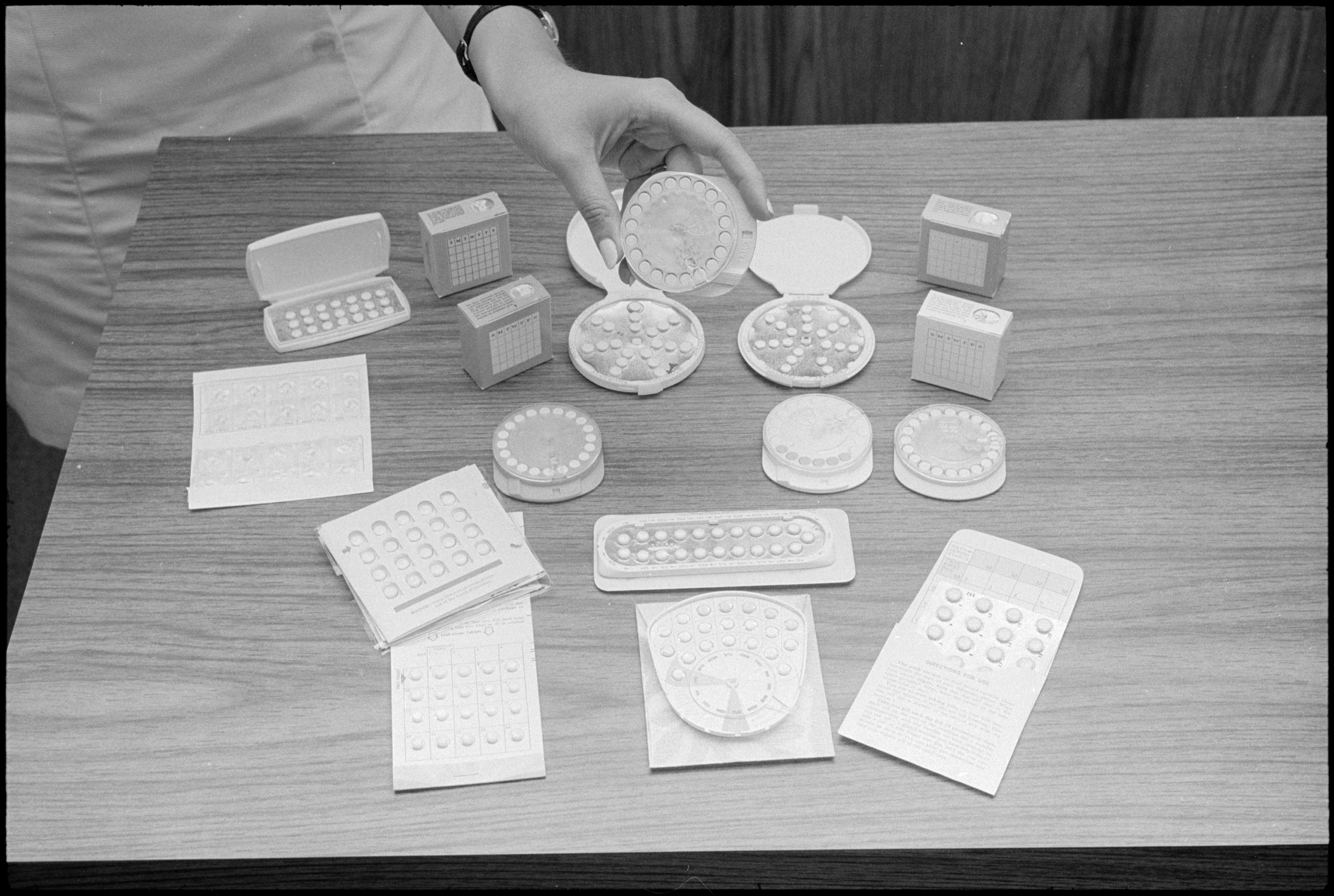 A person's hand displays various types of birth control pills and packaging on a table
