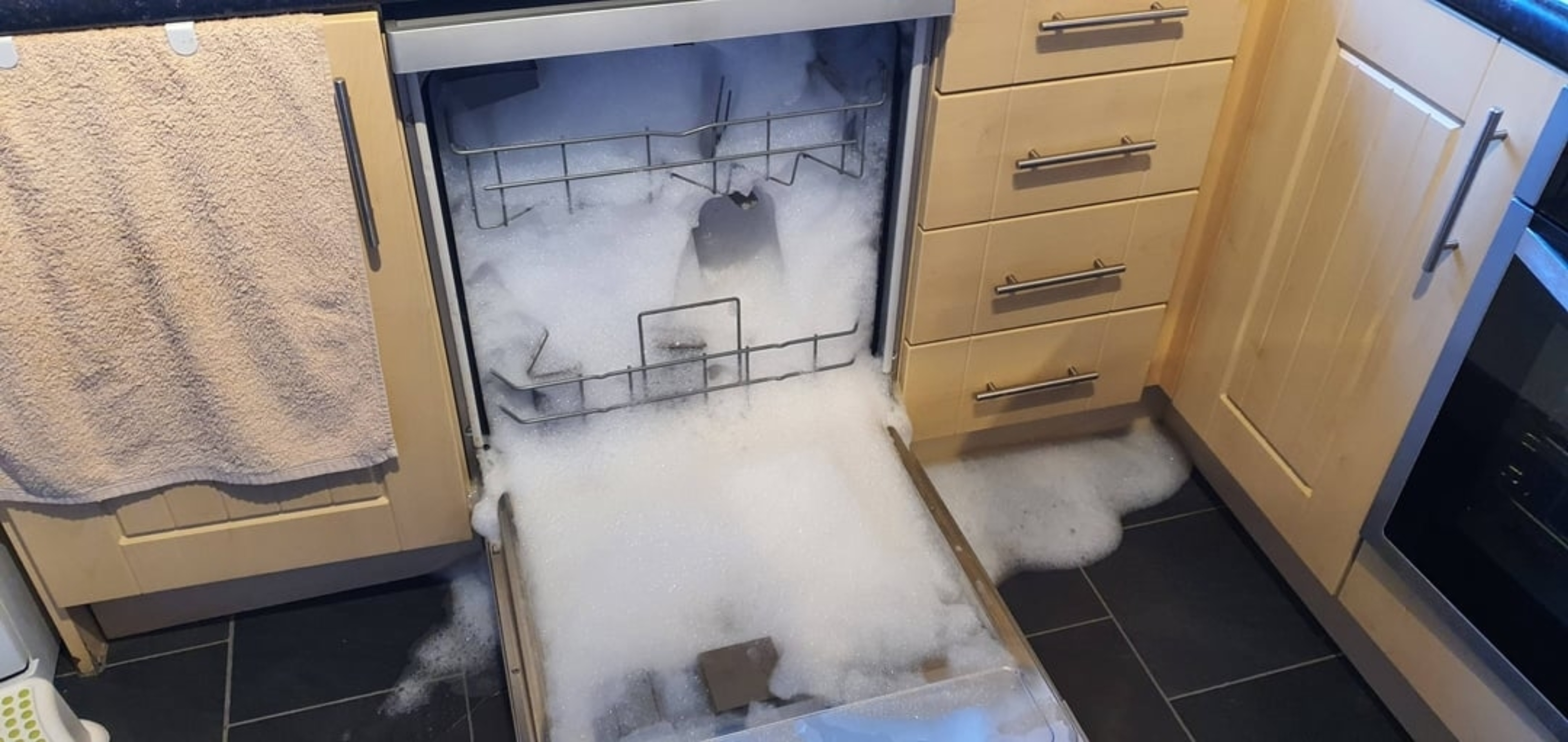 Dishwasher in a kitchen overflowing with soap suds, covering the floor