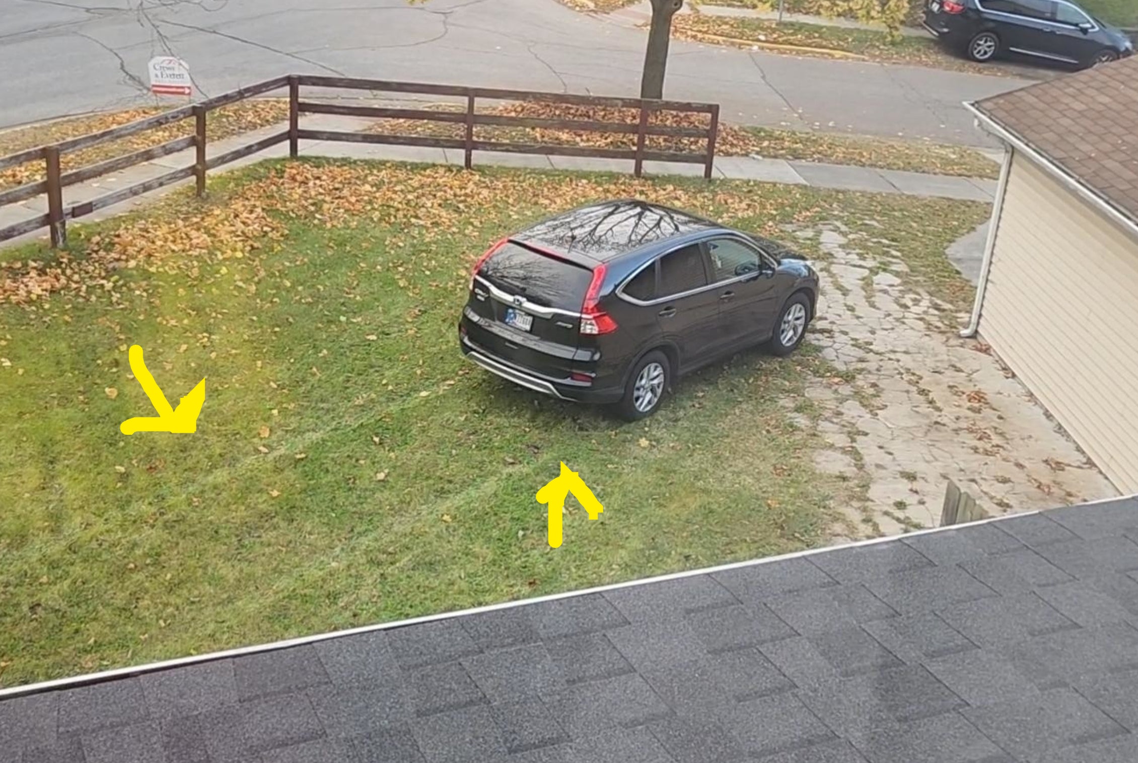 A car is parked on a grassy lawn next to a house, seen from an elevated view