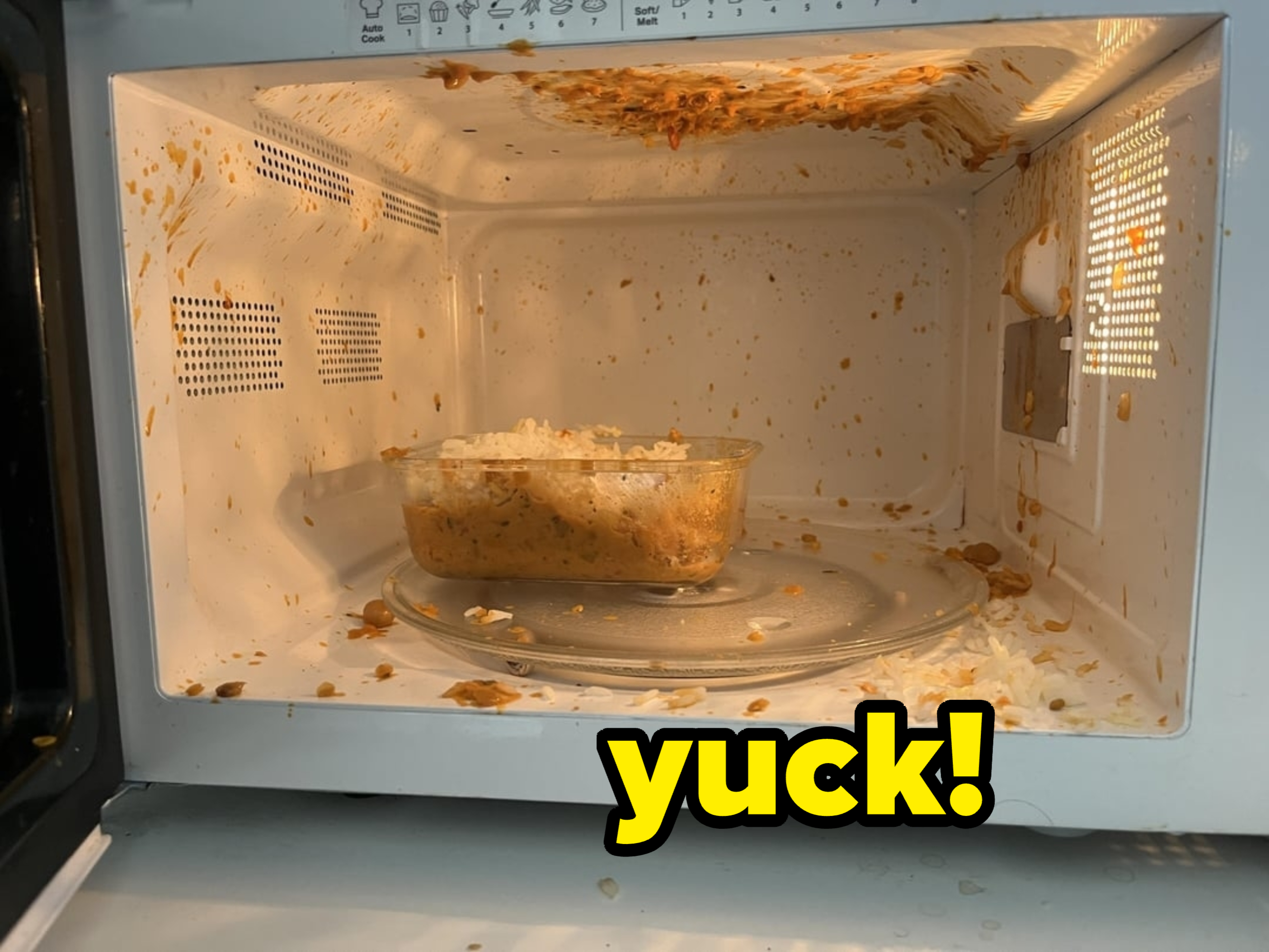 A microwave with food splattered all over the interior and a glass container of food on the rotating plate