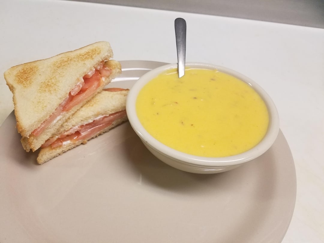 A plate with a grilled ham and cheese sandwich cut in half, next to a bowl of creamy soup with a spoon