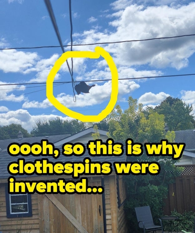 A black shirt hangs from a wire high above a backyard with a wooden fence and a small shed and text reads, "Oooh, so this is why clothespins were invented&hellip;"