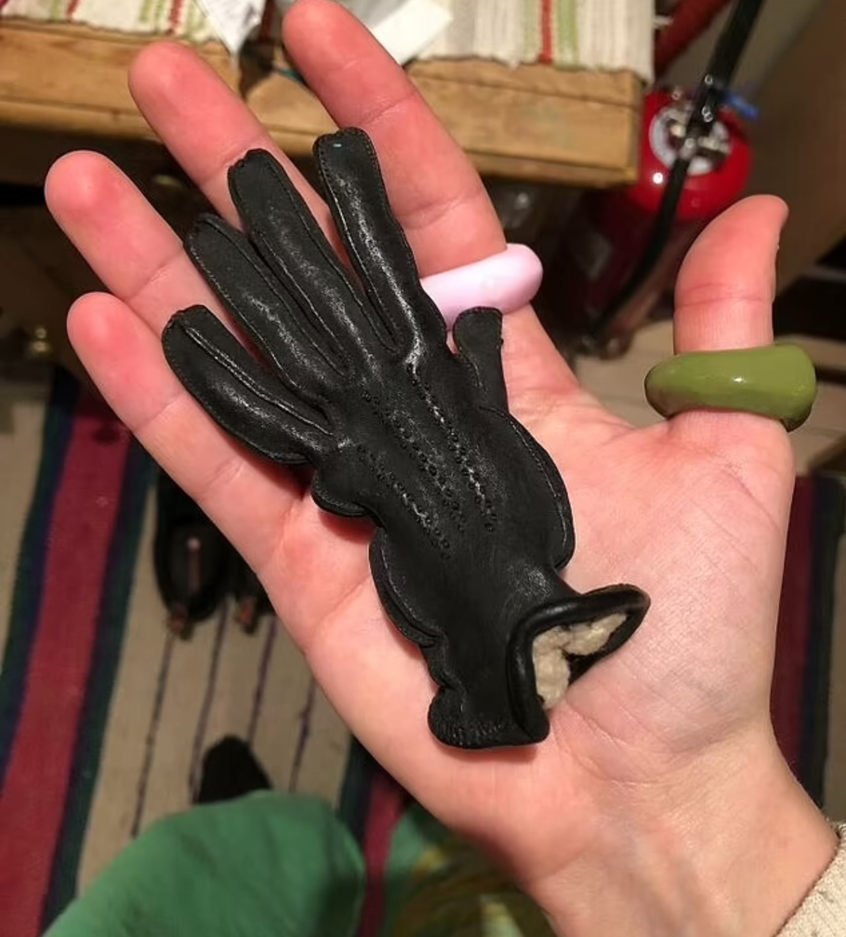 A hand holding a shrunken, black, fingerless leather glove with a plush beige lining