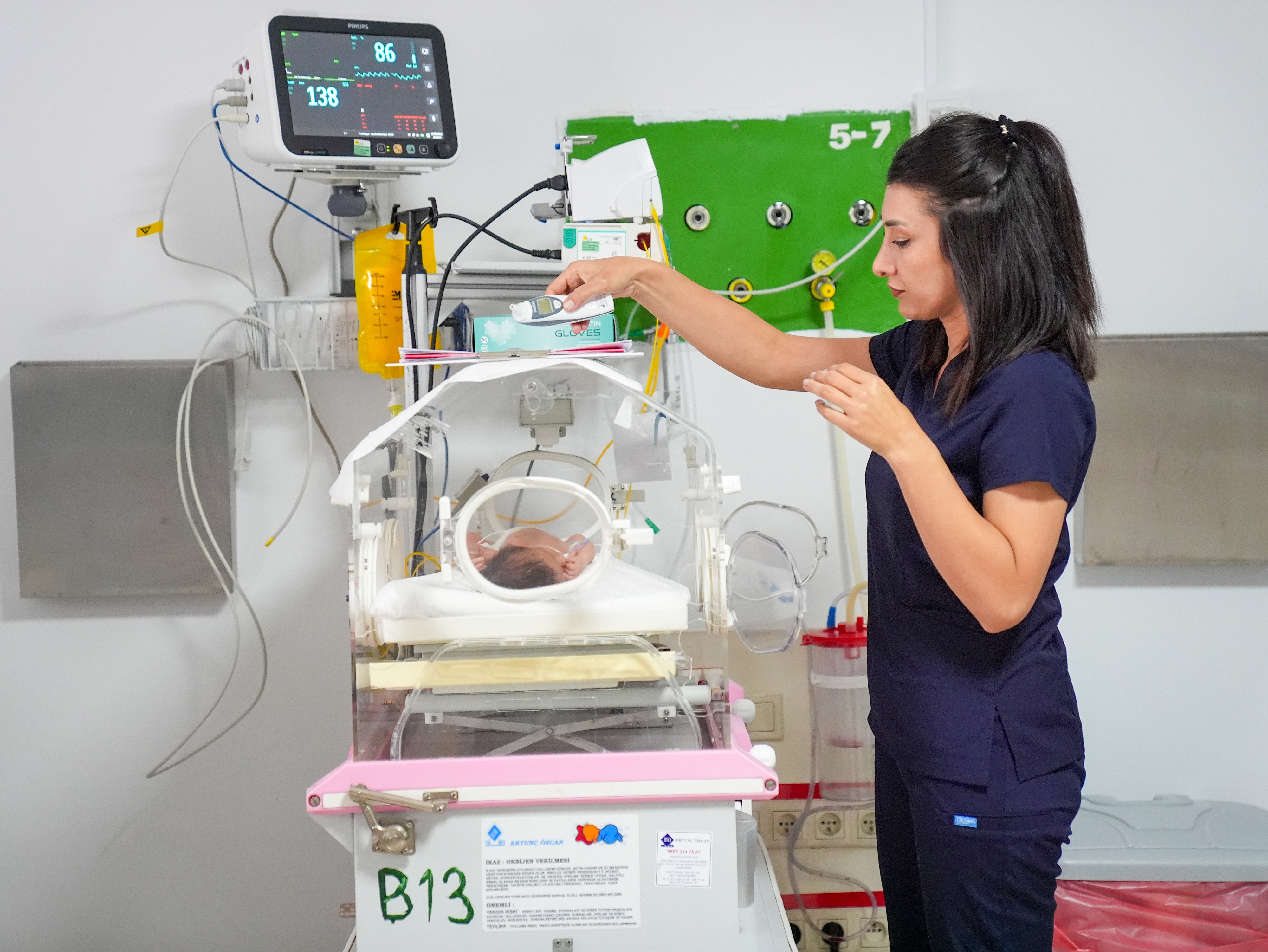 A nurse adjusts medical equipment for a newborn baby in an incubator inside a hospital's neonatal intensive care unit (NICU)