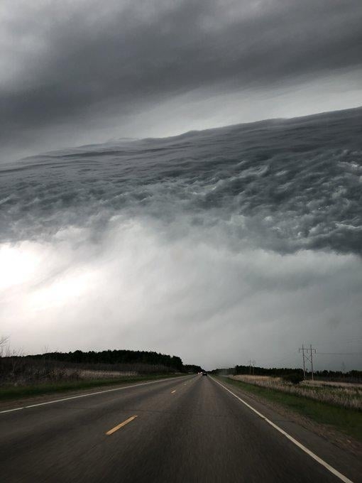 A deserted road stretches into the distance under an ominous sky filled with dramatic, swirling clouds