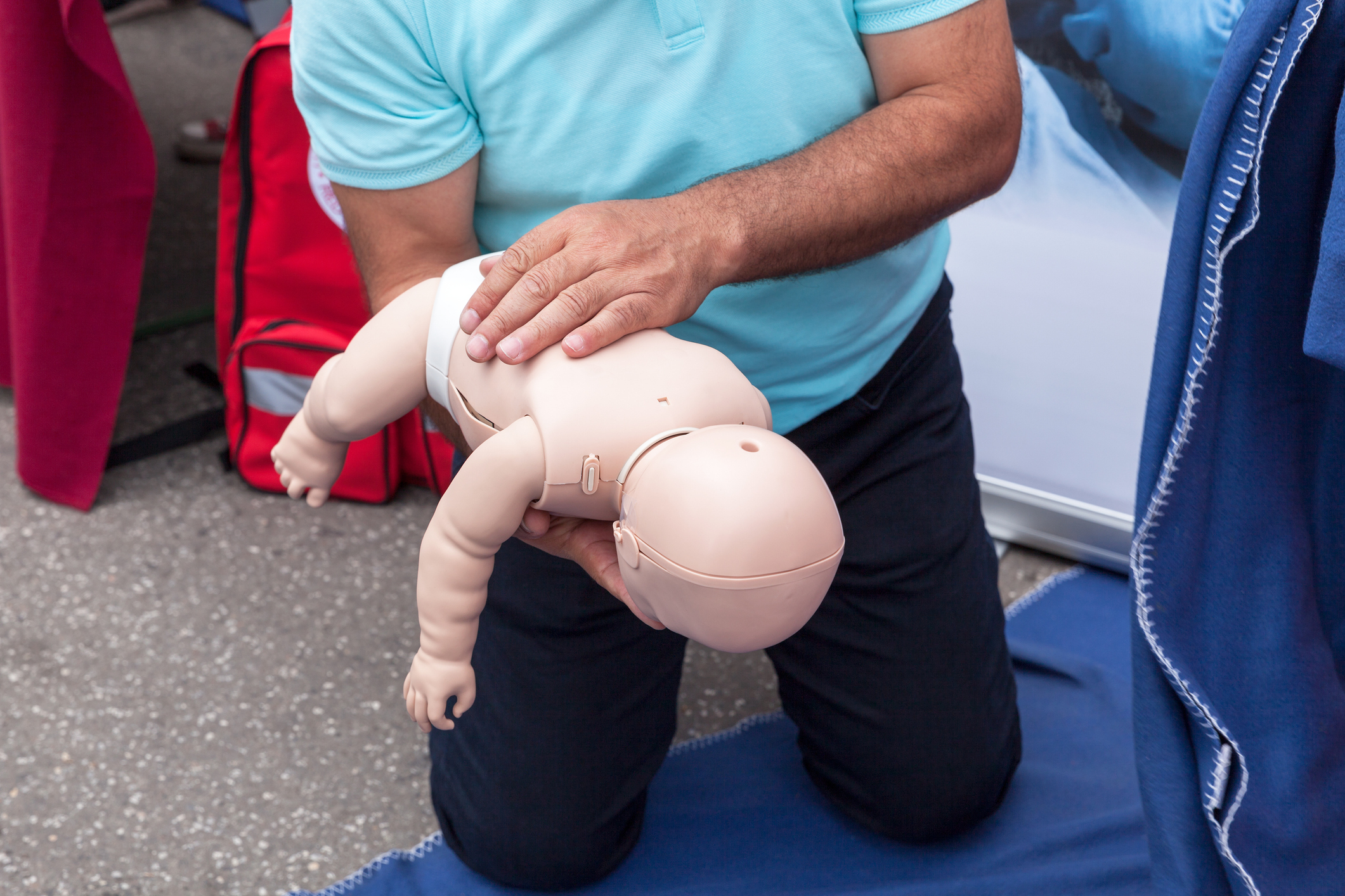 Person demonstrates infant CPR technique using a baby mannequin placed on their knee