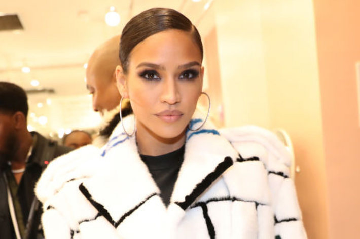 Cassie Ventura at an event, wearing a fashionable fur coat with geometric patterns and large hoop earrings