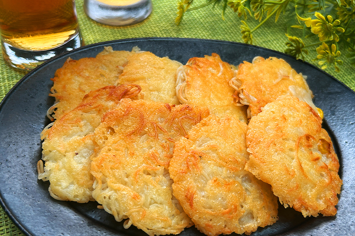 緑のテーブルクロスに置かれたお皿に盛り付けられた数枚のカリカリに揚げたそうめん。バックには飲み物と黄色い花が飾られている。