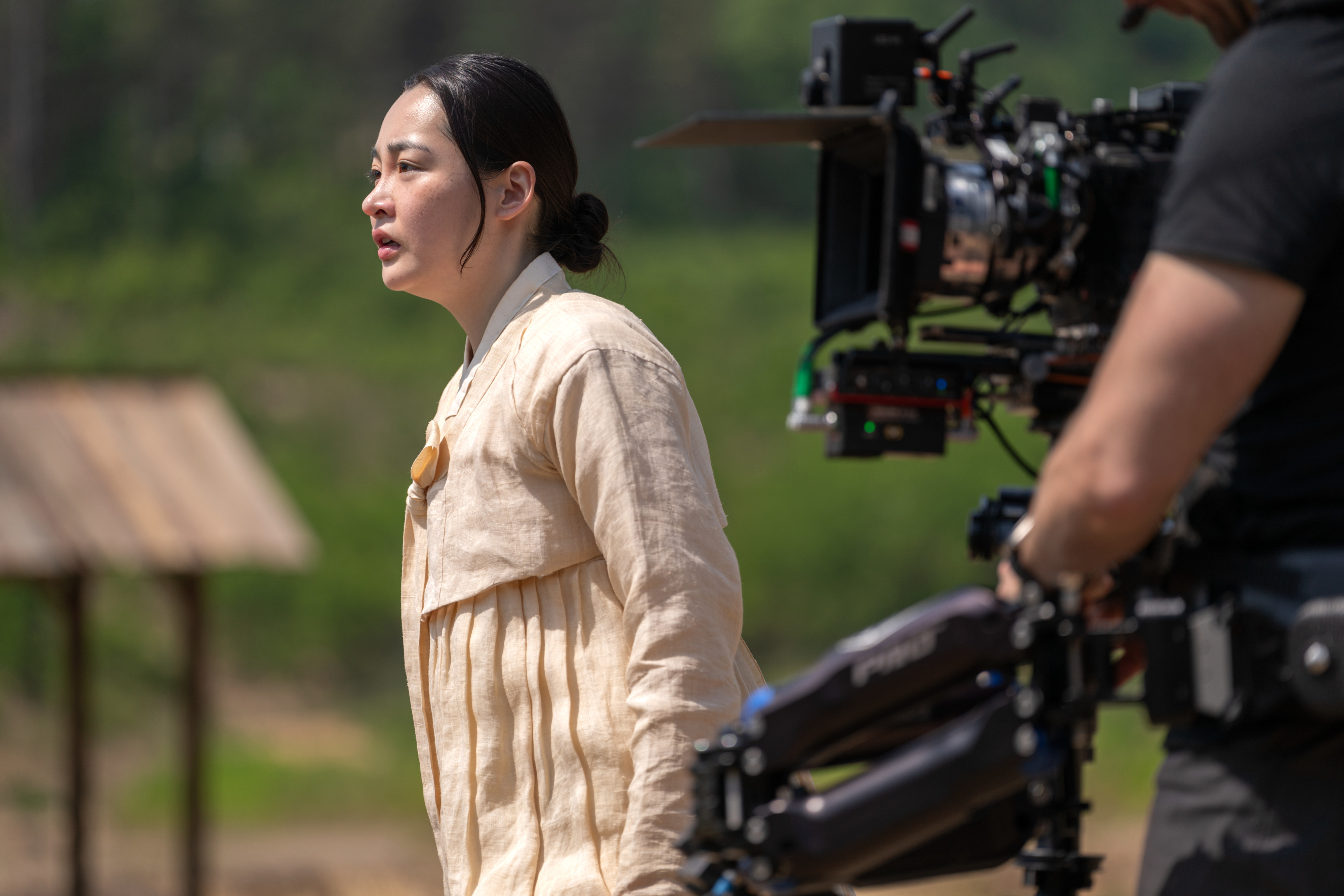 The image shows a behind-the-scenes moment on a TV show set, featuring an actress in traditional attire performing a scene, with a cameraman filming her