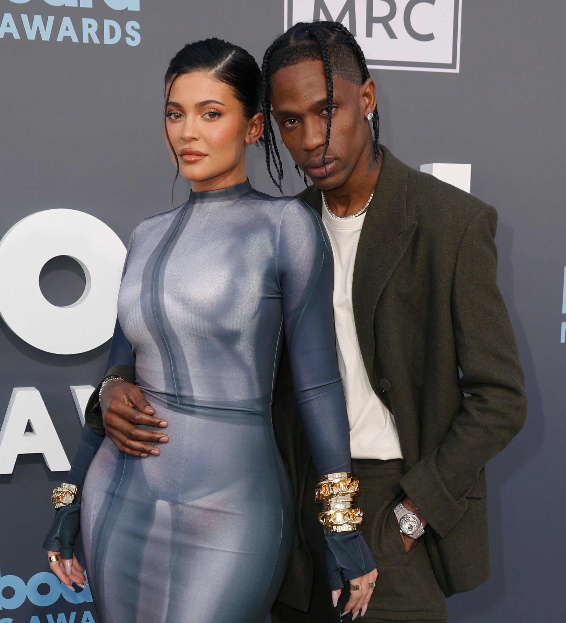 Kylie Jenner in a form-fitting dress and Travis Scott in a dark suit pose together on the red carpet at the Billboard Music Awards