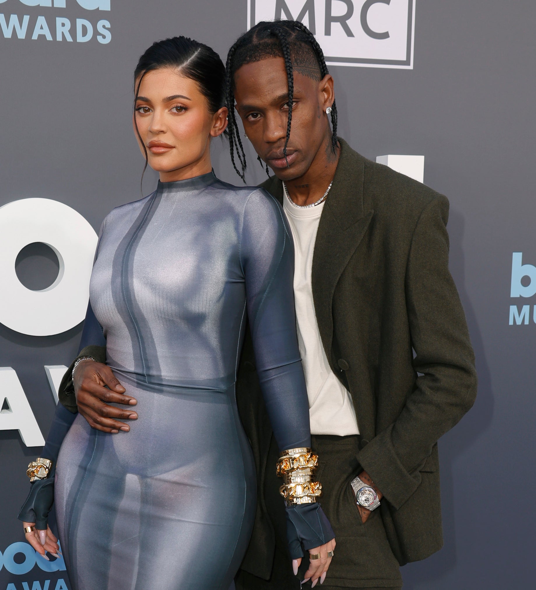 Kylie Jenner in a form-fitting dress and Travis Scott in a dark suit pose together on the red carpet at the Billboard Music Awards