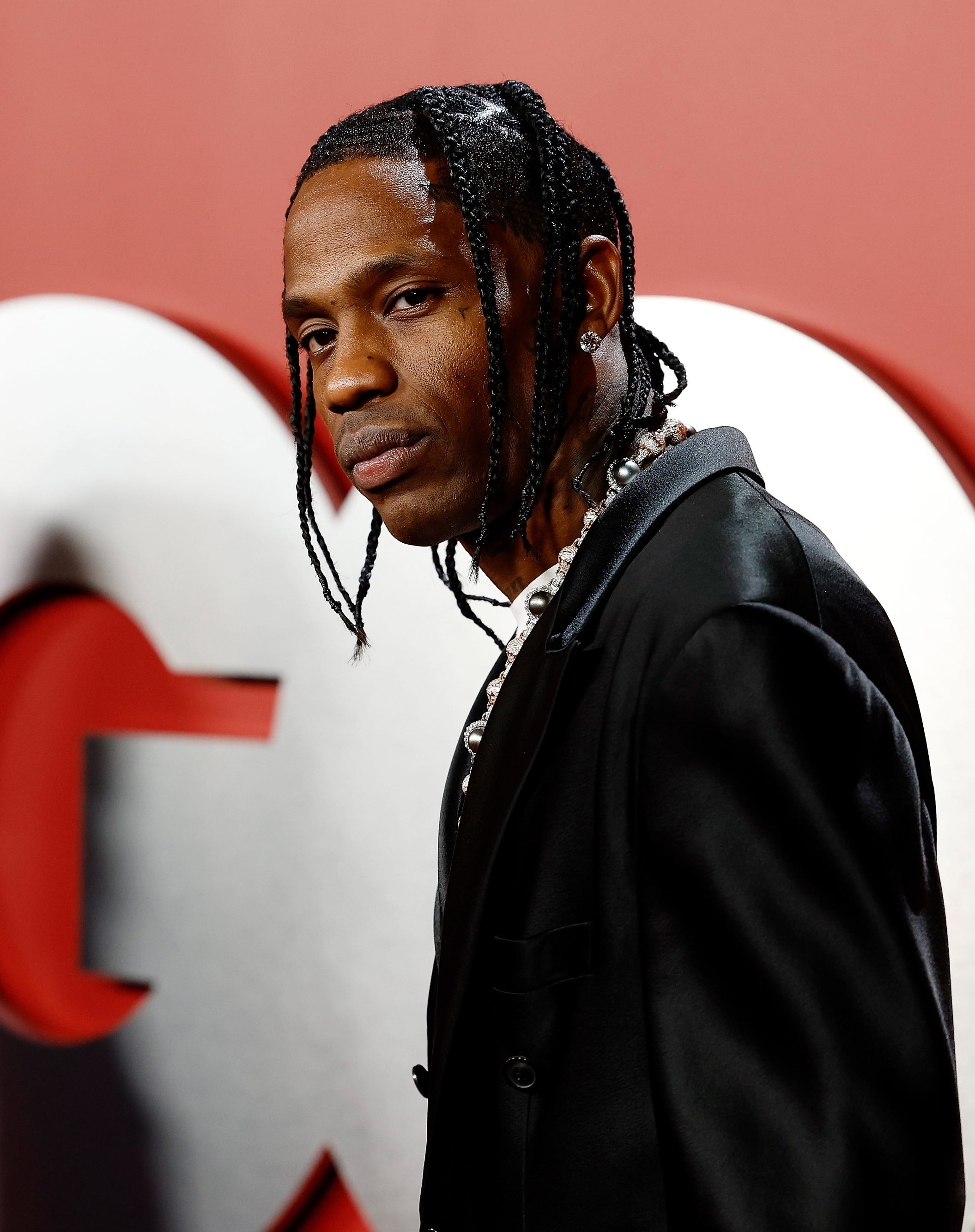 Travis Scott wearing a stylish black suit with braided hair stands in front of a GQ backdrop