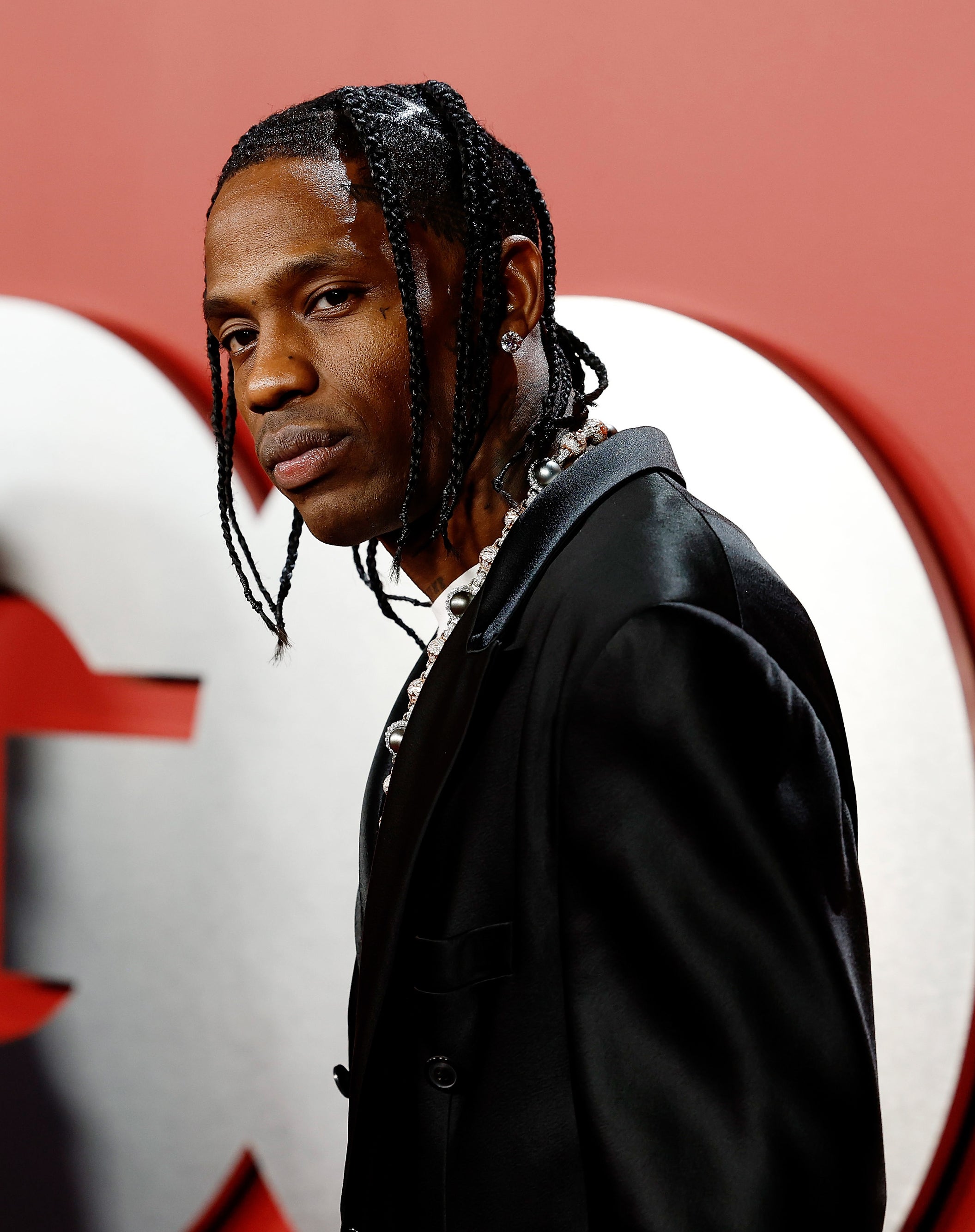 Travis Scott wearing a stylish black suit with braided hair stands in front of a GQ backdrop