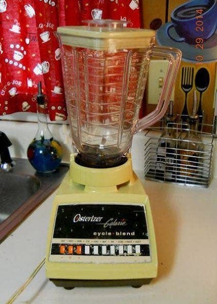 A vintage Osterizer Galaxie Cyclo Blend blender on a kitchen counter with a sink and utensils in the background